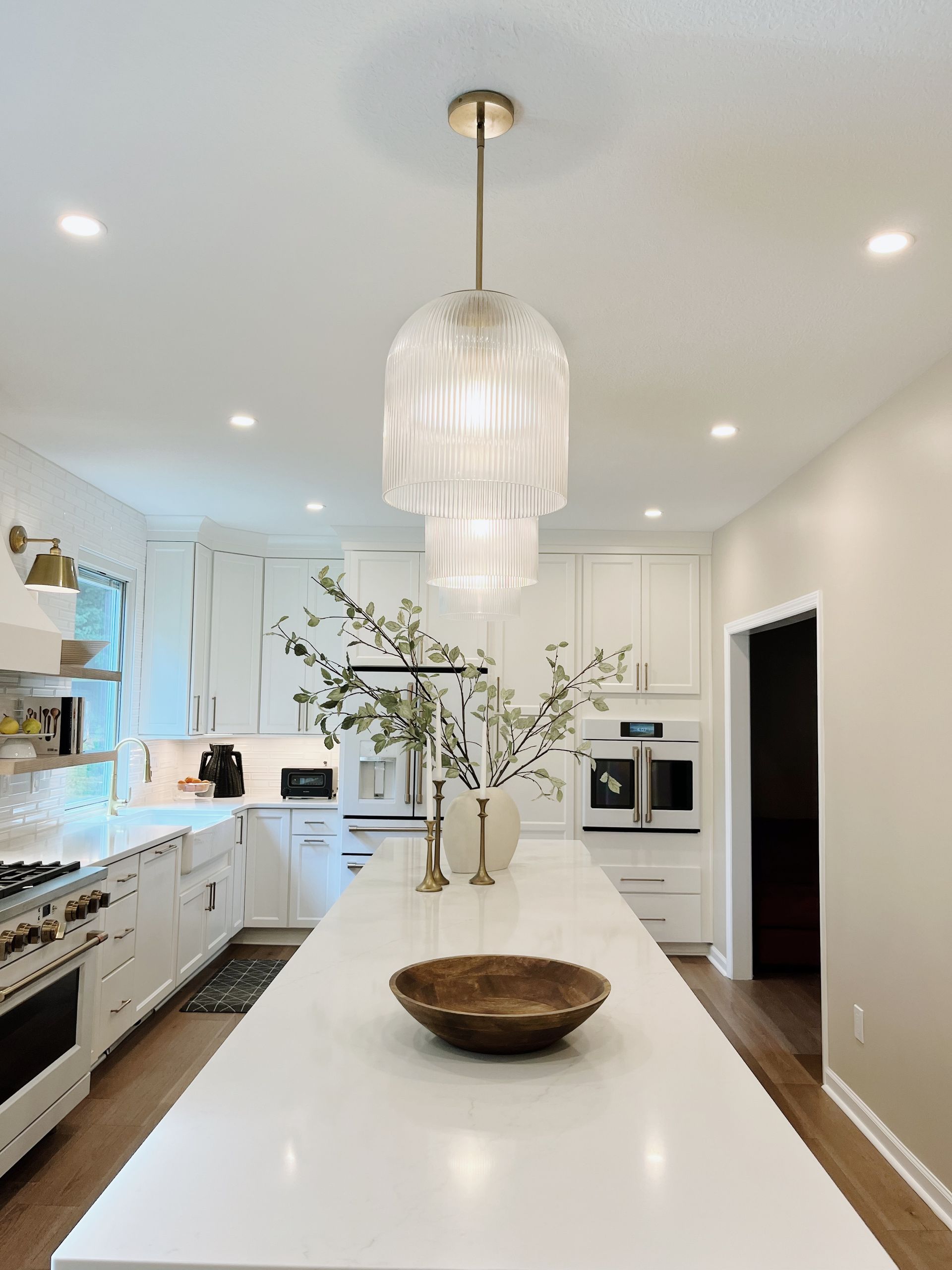 Bright modern white kitchen with a large island, pendant light, and vase of flowers