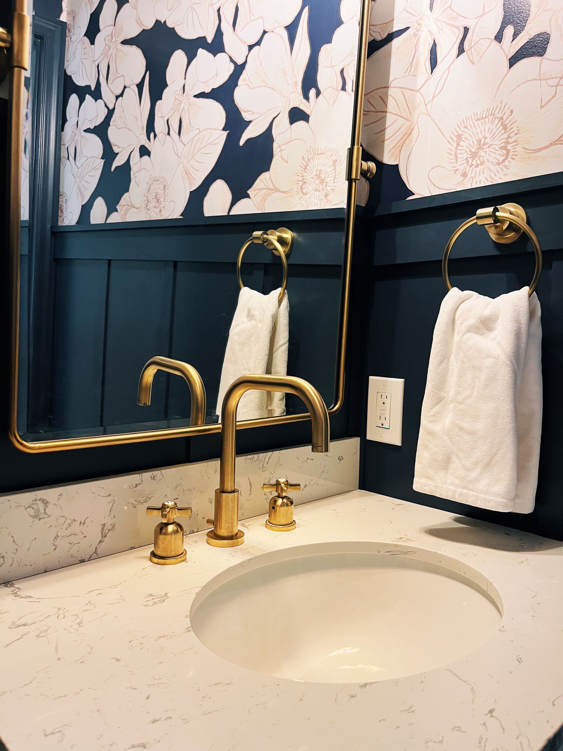 Bathroom vanity with gold faucet, white sink, navy and white wall panels, and towel hanging on a ring