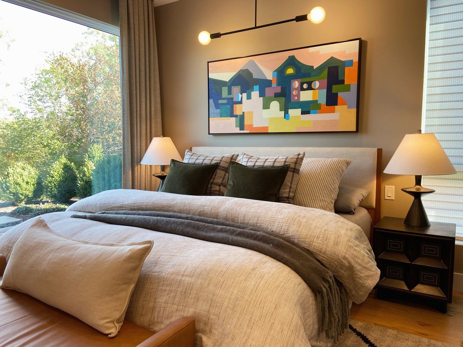 Cozy bedroom with a neatly made bed, beige decor, bedside lamps, and colorful wall art by a window