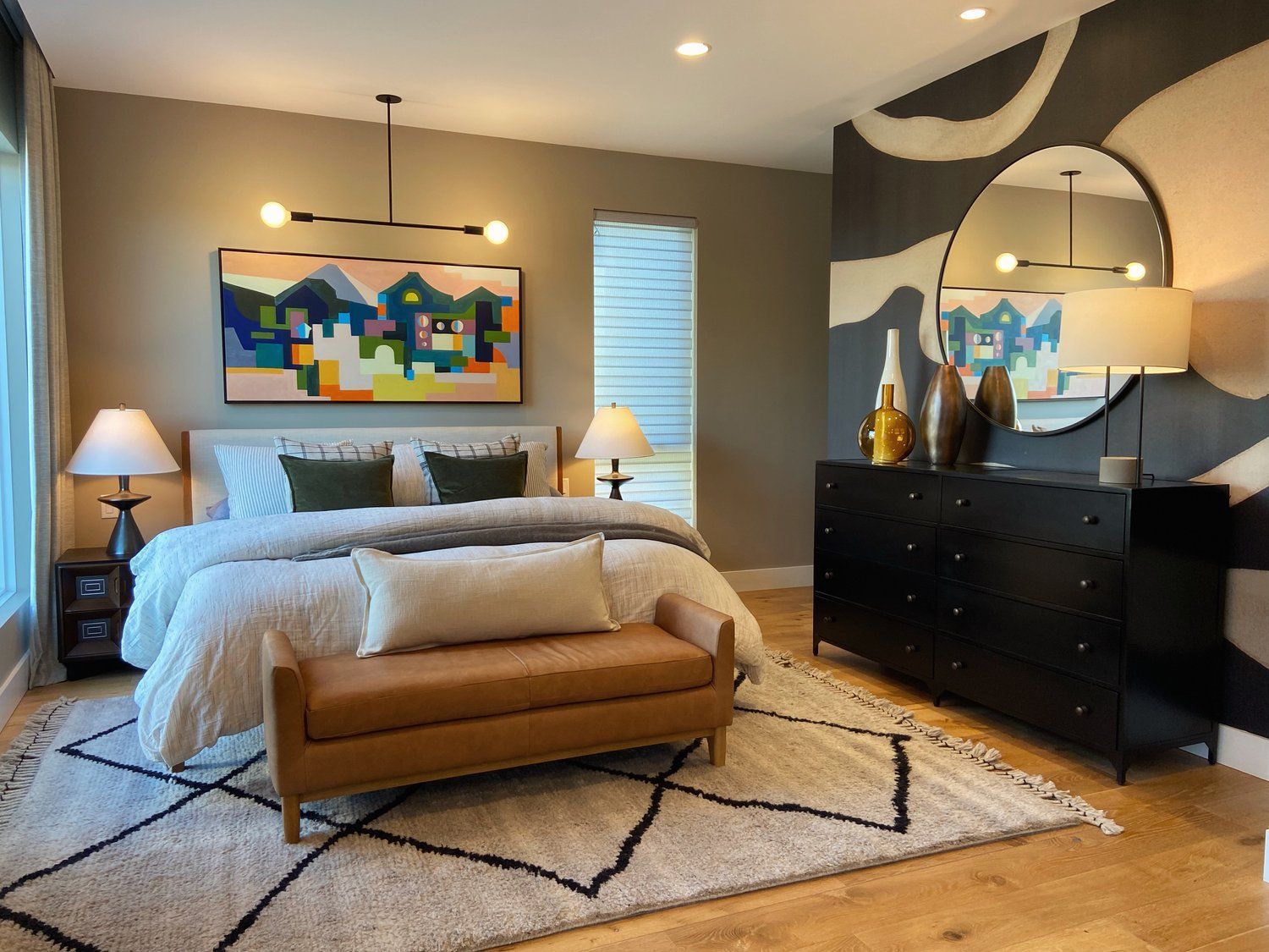 Modern bedroom with bed, bench, dresser, lamps, and colorful wall art on a patterned rug.
