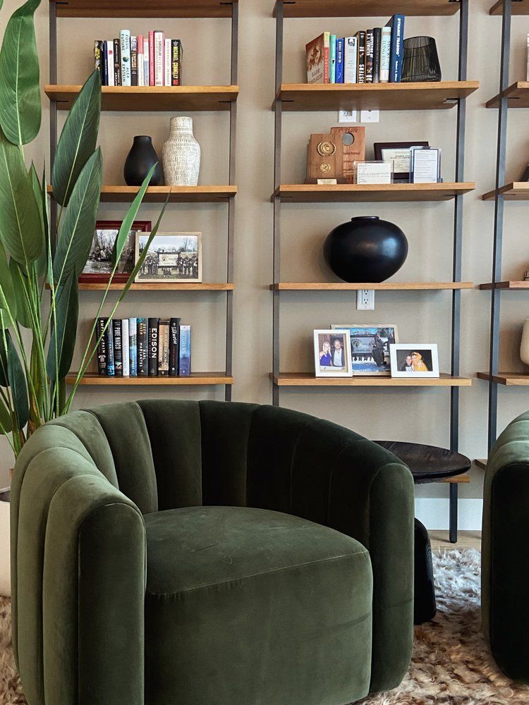 Green velvet chair in a stylish living room with wooden shelves, books, plants, and framed photos.