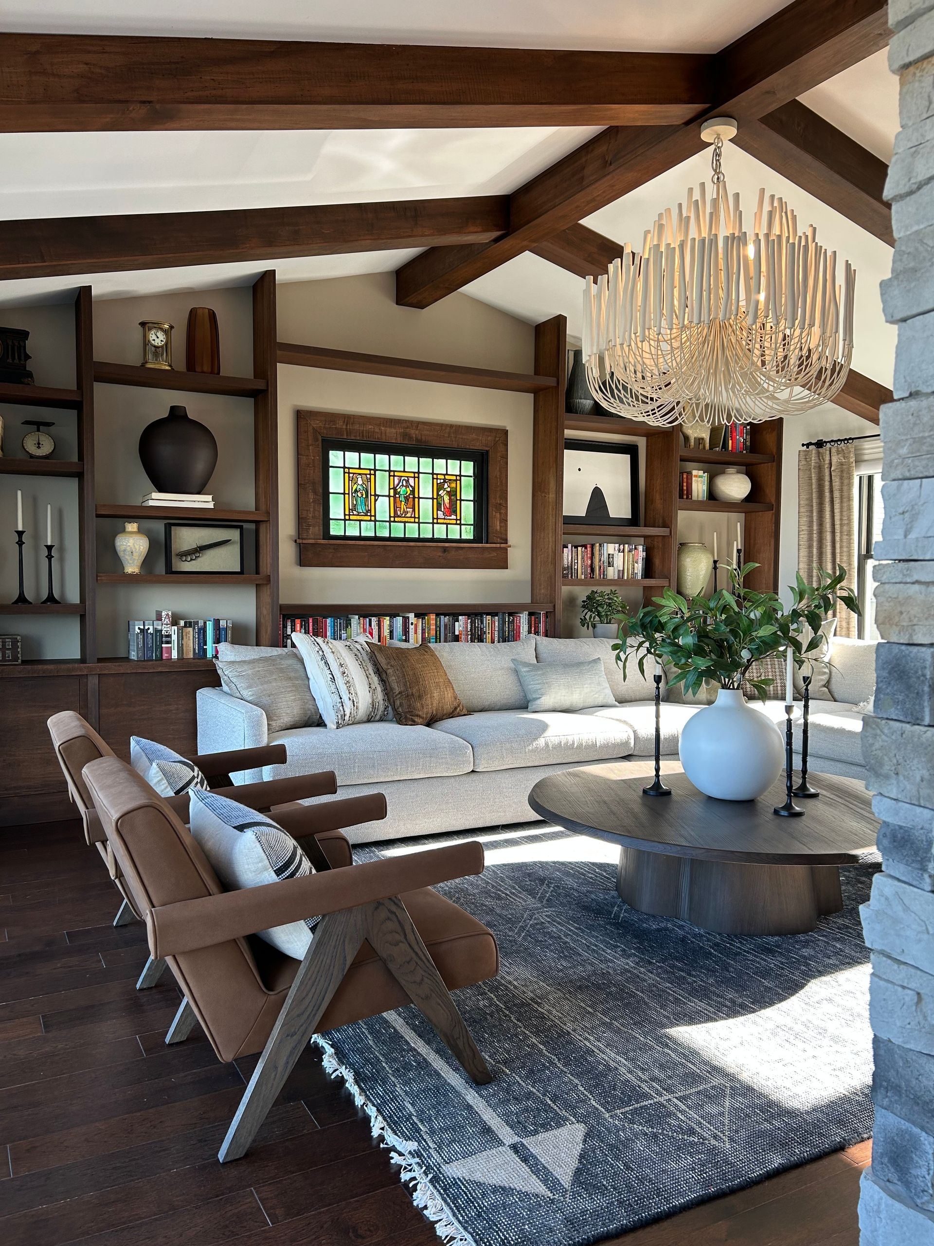 Rustic living room with exposed beams, stone fireplace, sectional sofa, chandelier, and large round coffee table