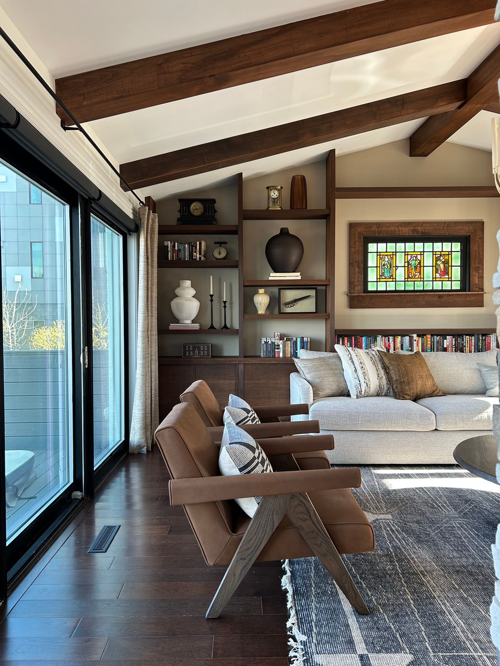 Modern living room with wood beams, large windows, beige sofa, and built-in shelves with decor