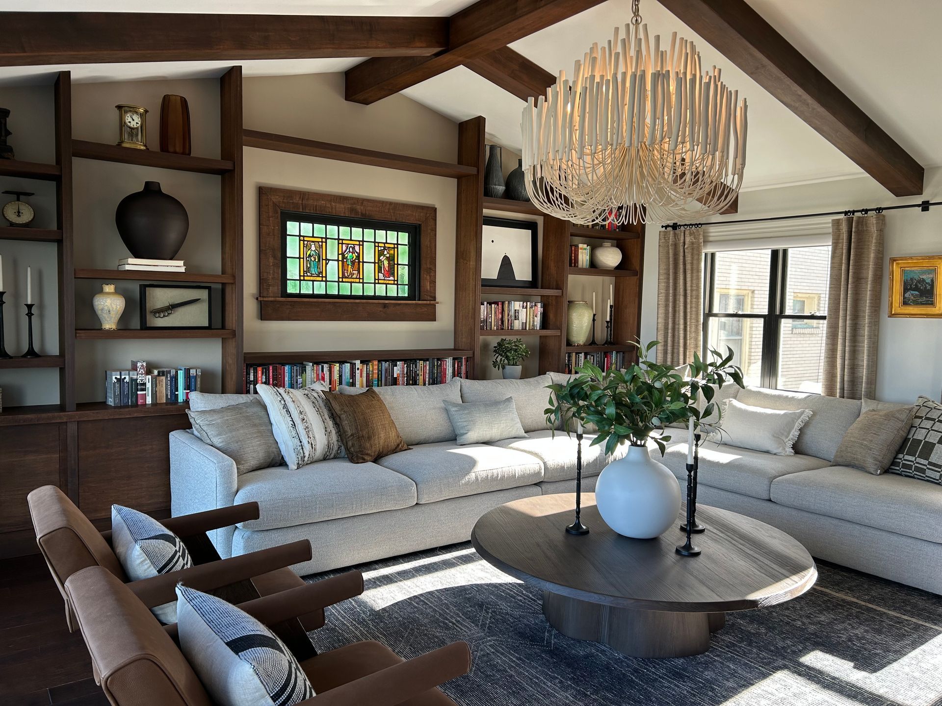 Bright living room with sectional sofas, round coffee table, wood beams, and a large chandelier