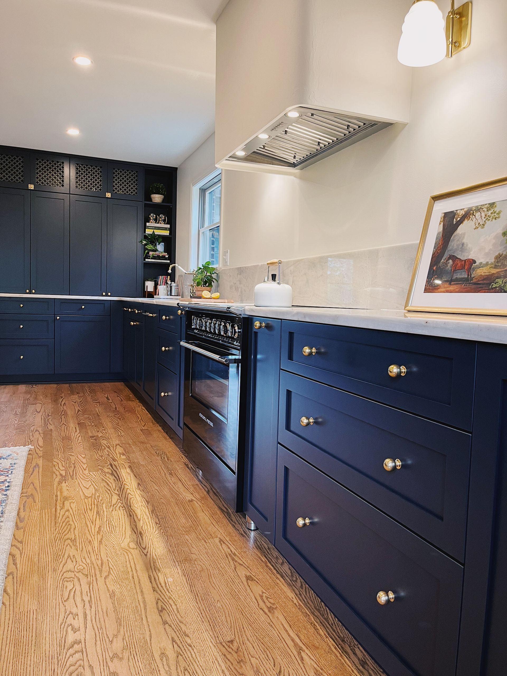 Navy blue galley kitchen with white countertops, stainless range hood, and wood floor