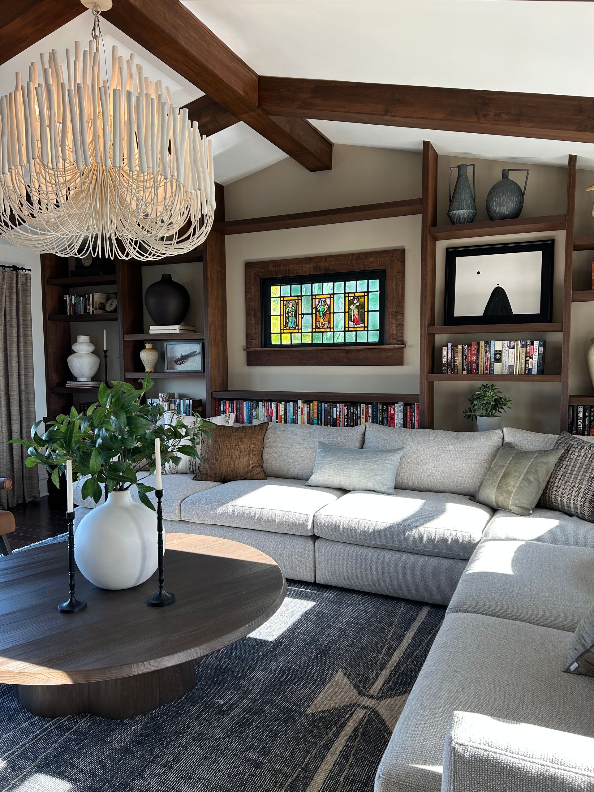 Elegant living room with chandelier, sectional sofa, wooden beams, and stained-glass window