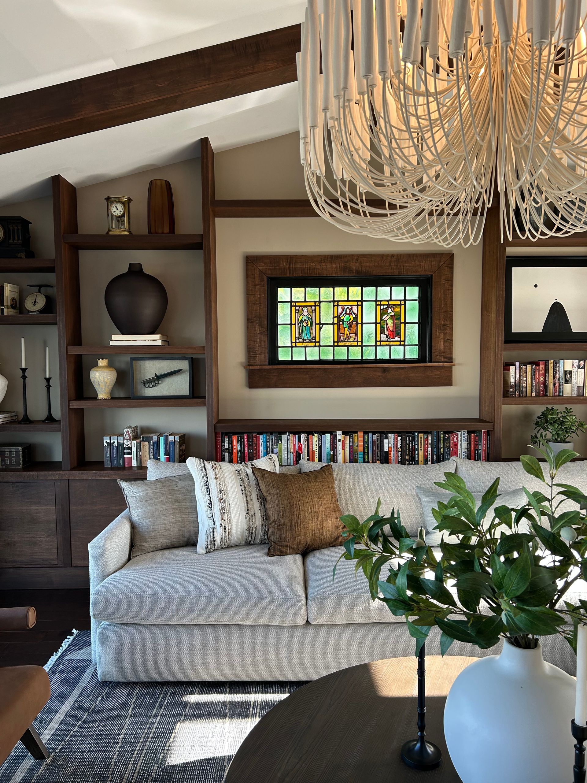 Cozy living room with bookshelf wall, stained-glass window, chandelier, and gray sofa with pillows