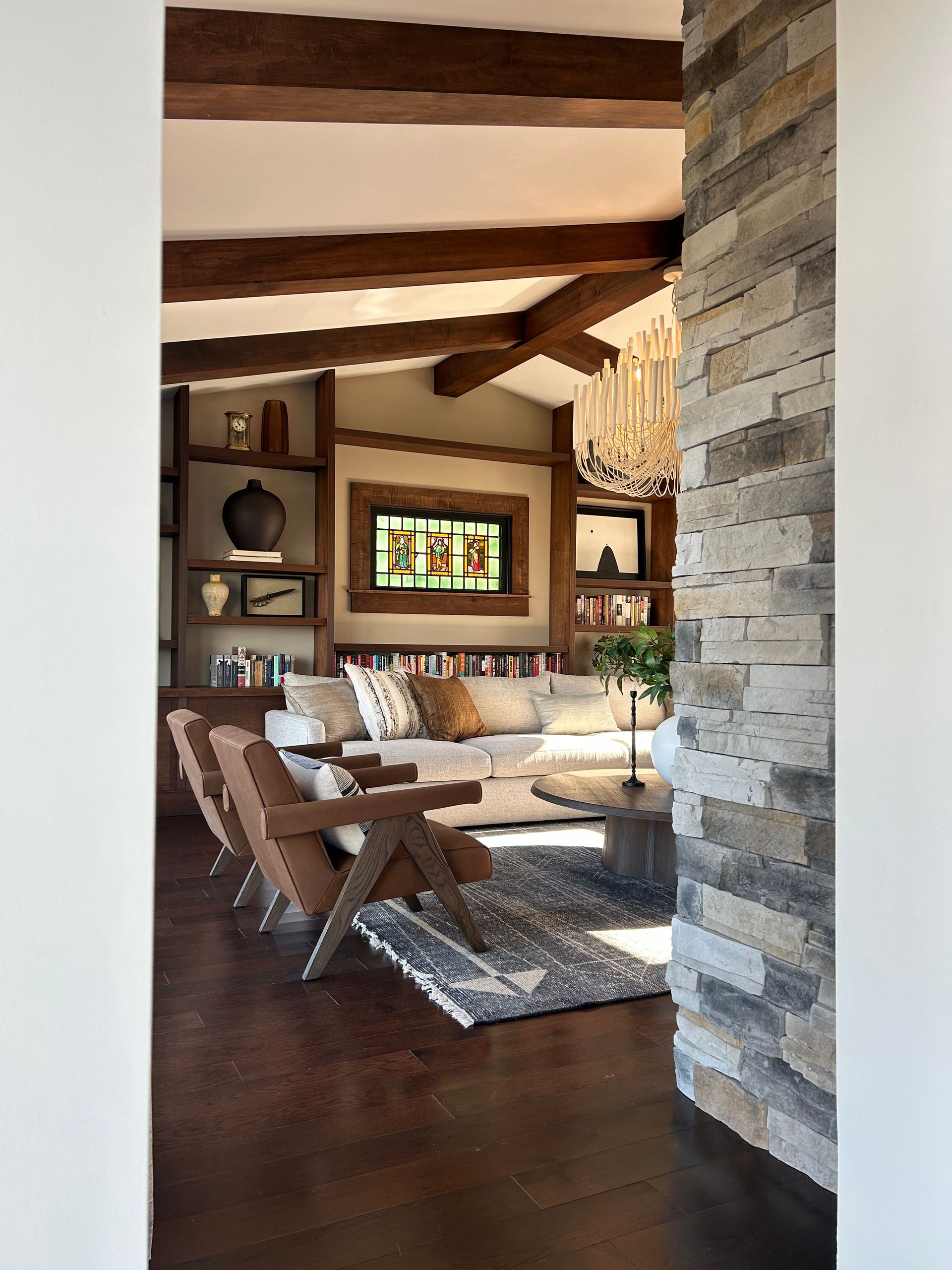 Rustic living room with exposed beams, stone fireplace, and wood furniture seen through a doorway