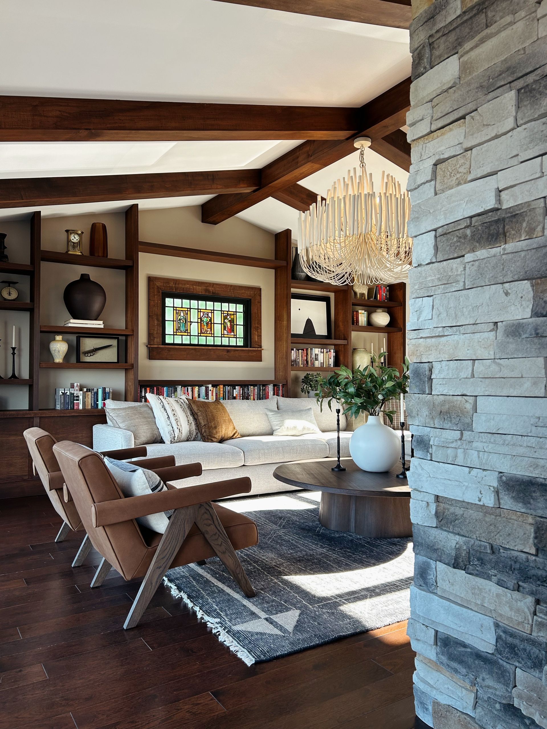 Cozy living room with exposed beams, stone accent wall, chandelier, and neutral sofas around a coffee table