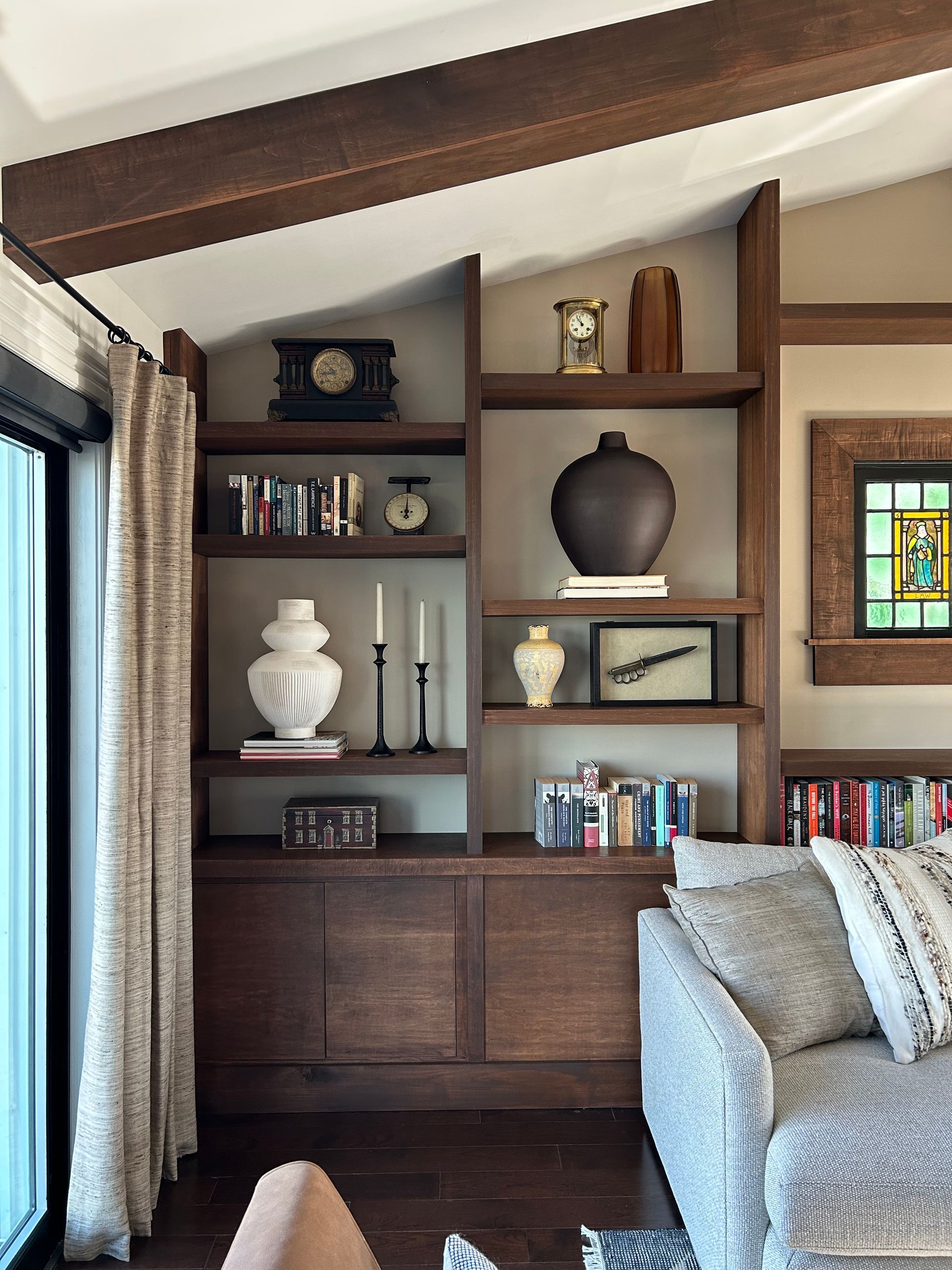 Built-in bookshelf with vases and books beside a window, next to a gray sofa in a cozy living room.