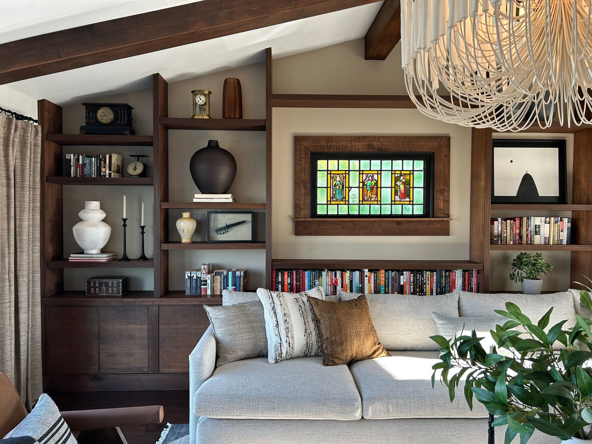 Cozy living room with gray sofa, built-in bookshelves, stained-glass window, and large chandelier