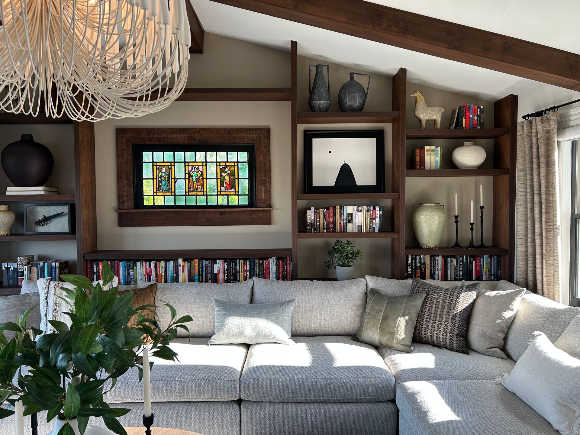 Cozy living room with gray sectional, built-in shelves, stained-glass window, and chandelier.
