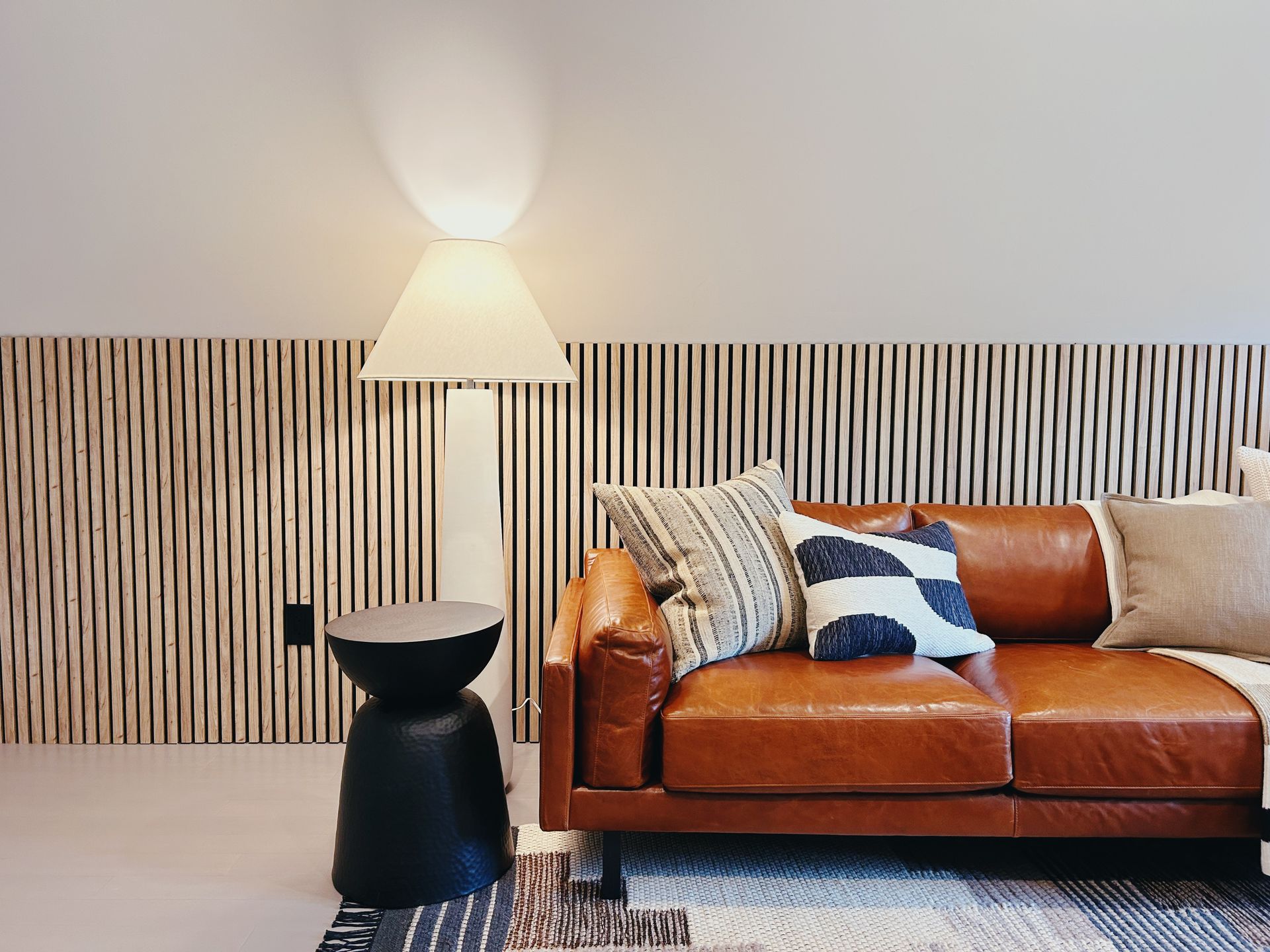Modern living room with brown leather sofa, striped wallpaper, floor lamp, and black side table