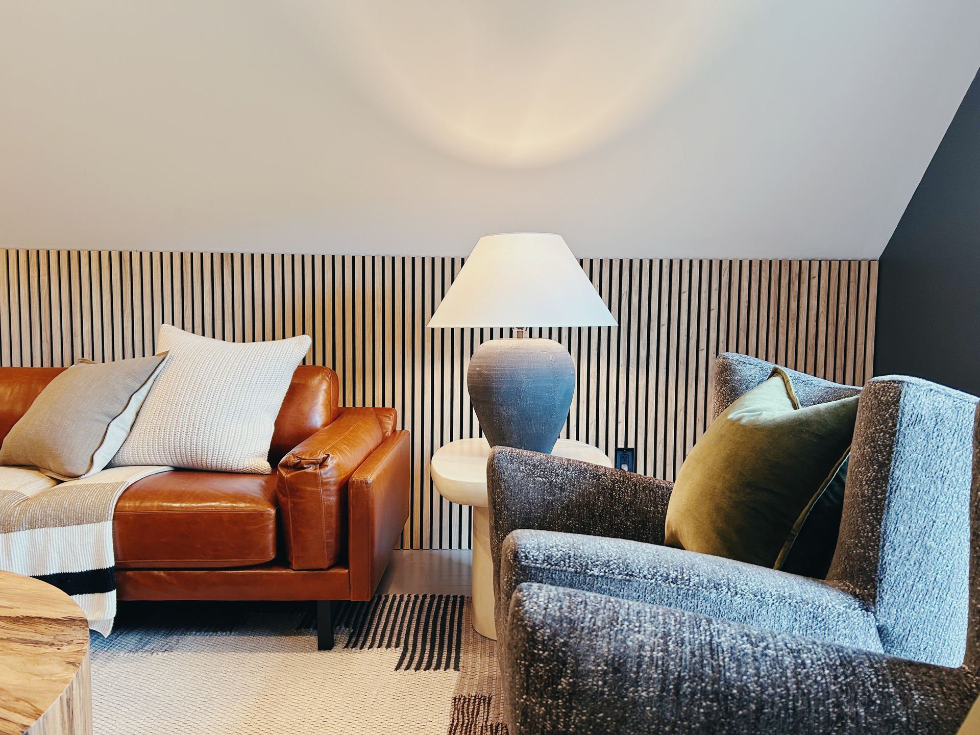 Cozy living room with leather and blue armchairs, lamp, striped wall, and sloped ceiling.
