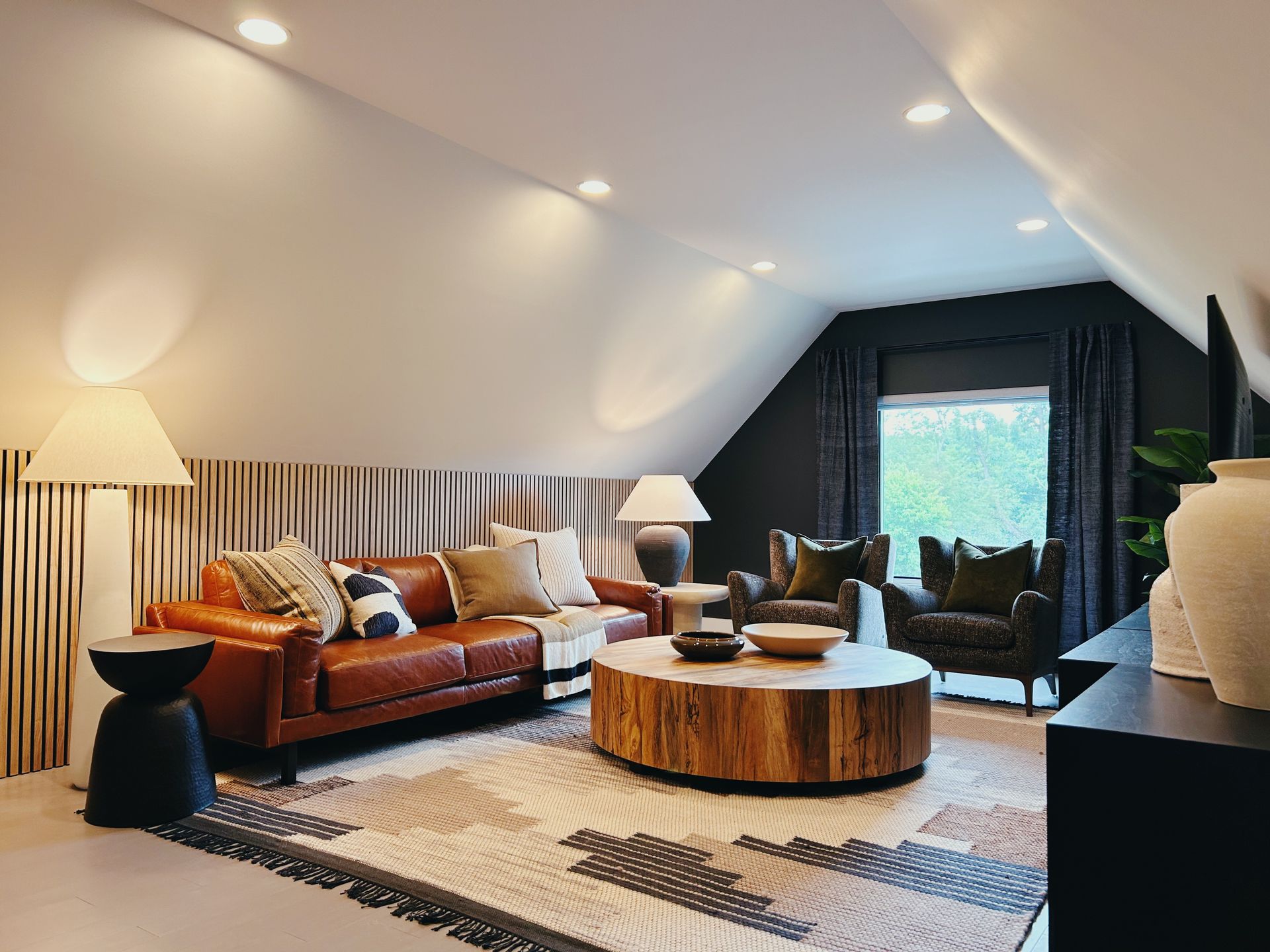 Stylish attic living room with leather sofa, armchairs, striped rug, and round wooden coffee table