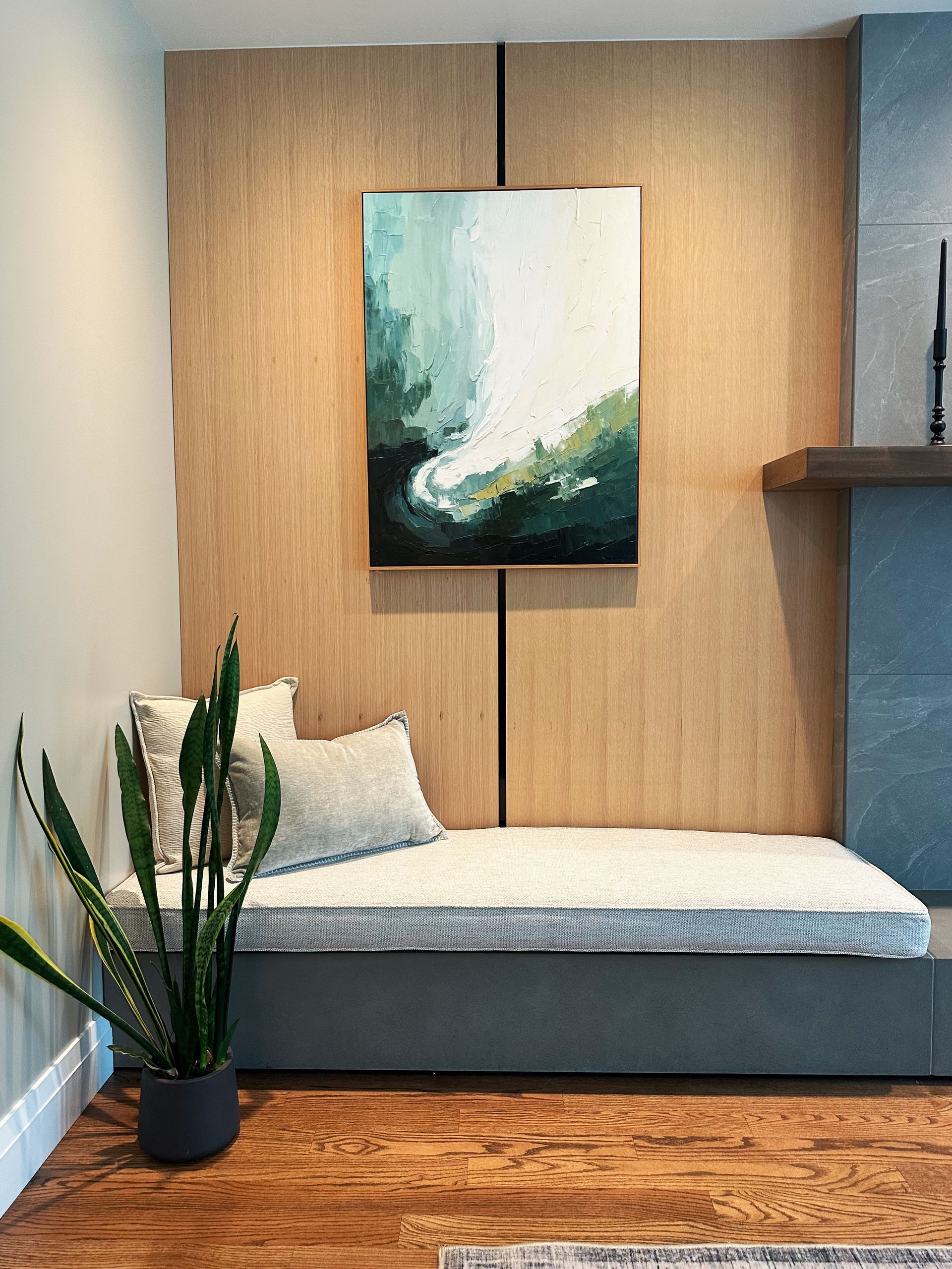 Modern living area with a gray daybed, abstract wall art, potted plant, and wood accents