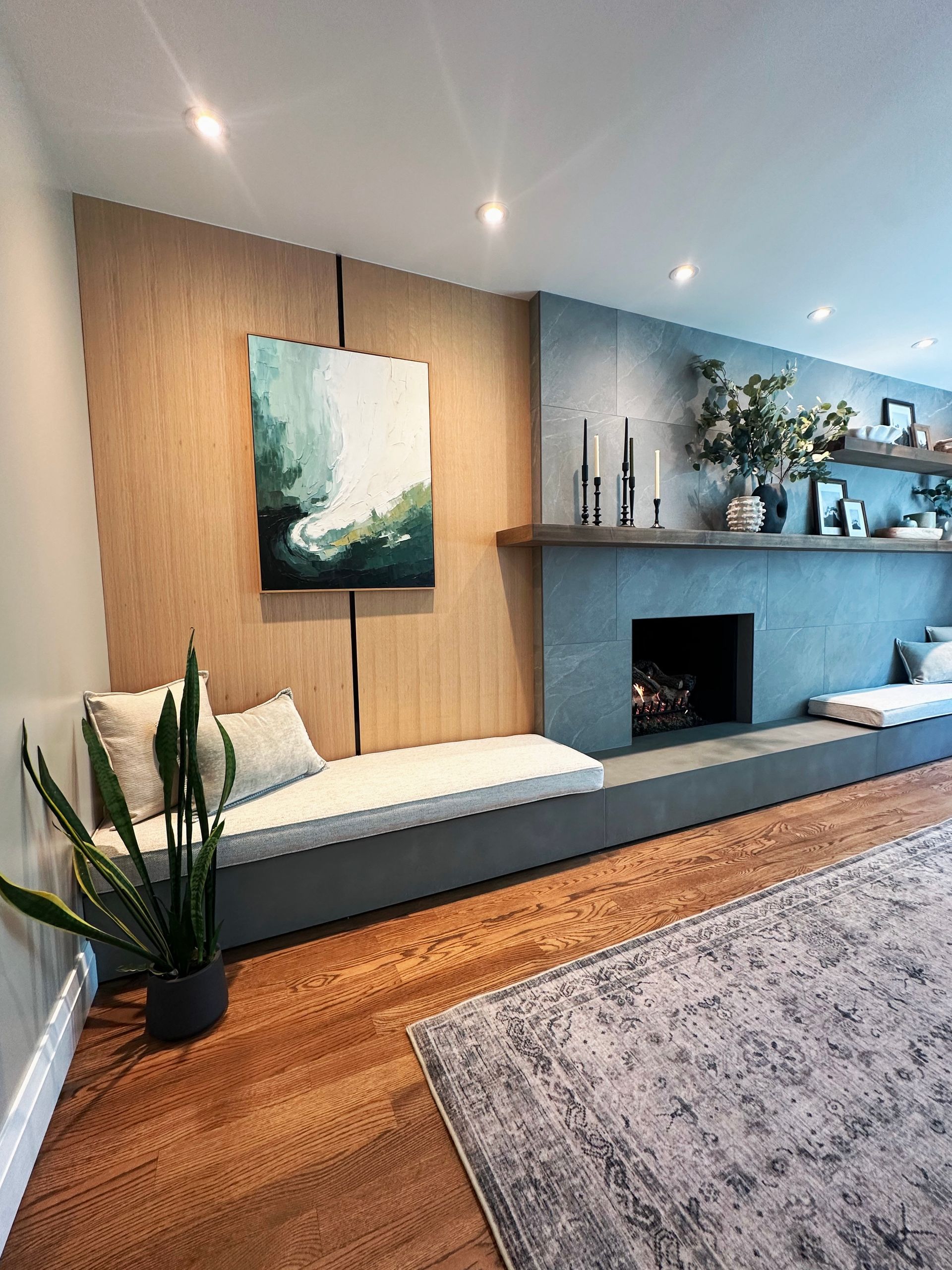 Modern living room with gray sofa, wood accent wall, fireplace, and abstract art under recessed lighting