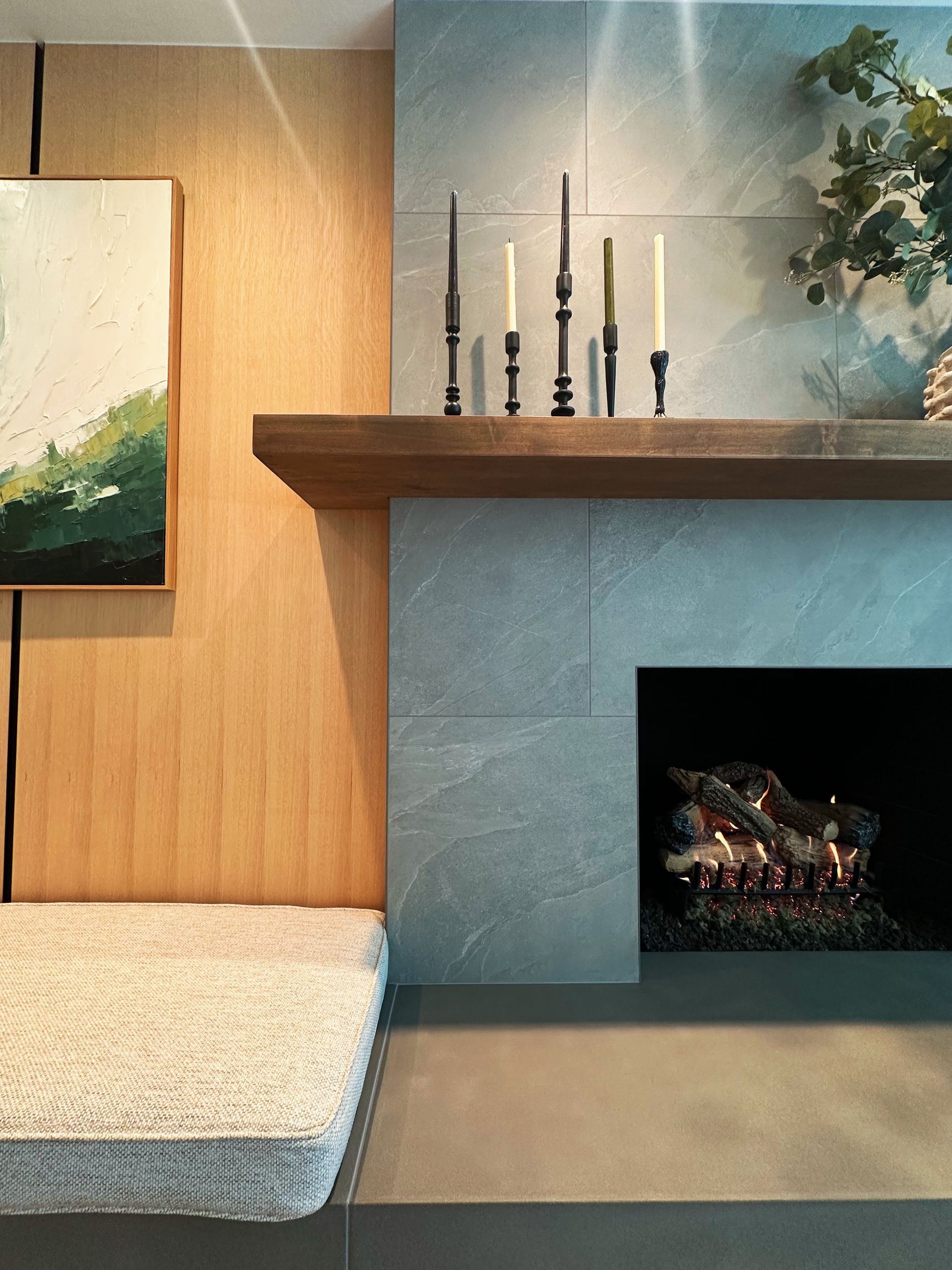 Modern living room with a fireplace, wood-paneled wall, artwork, and a white bench cushion