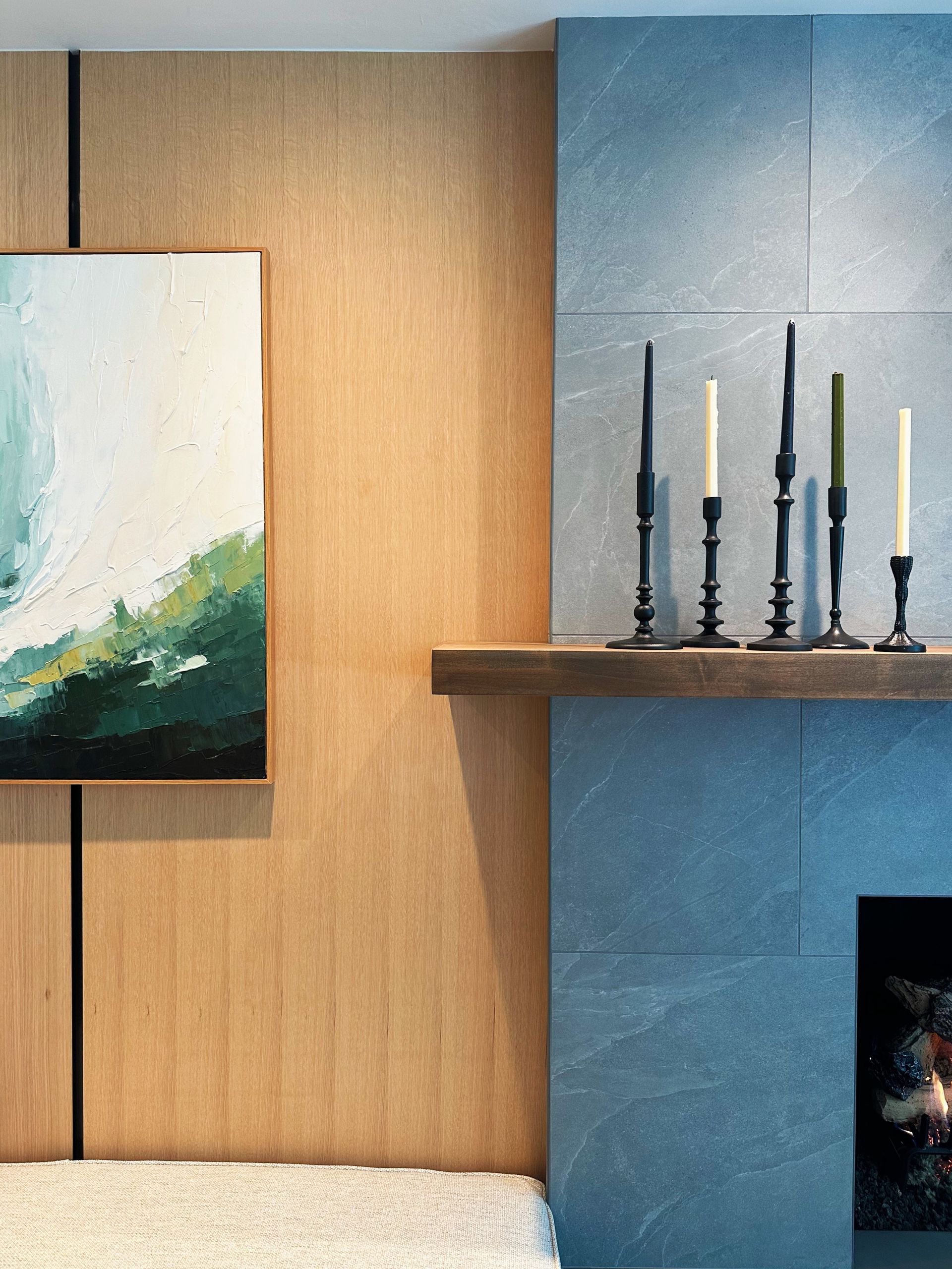 Modern living room wall with abstract painting, wooden paneling, blue fireplace, and candles on a shelf