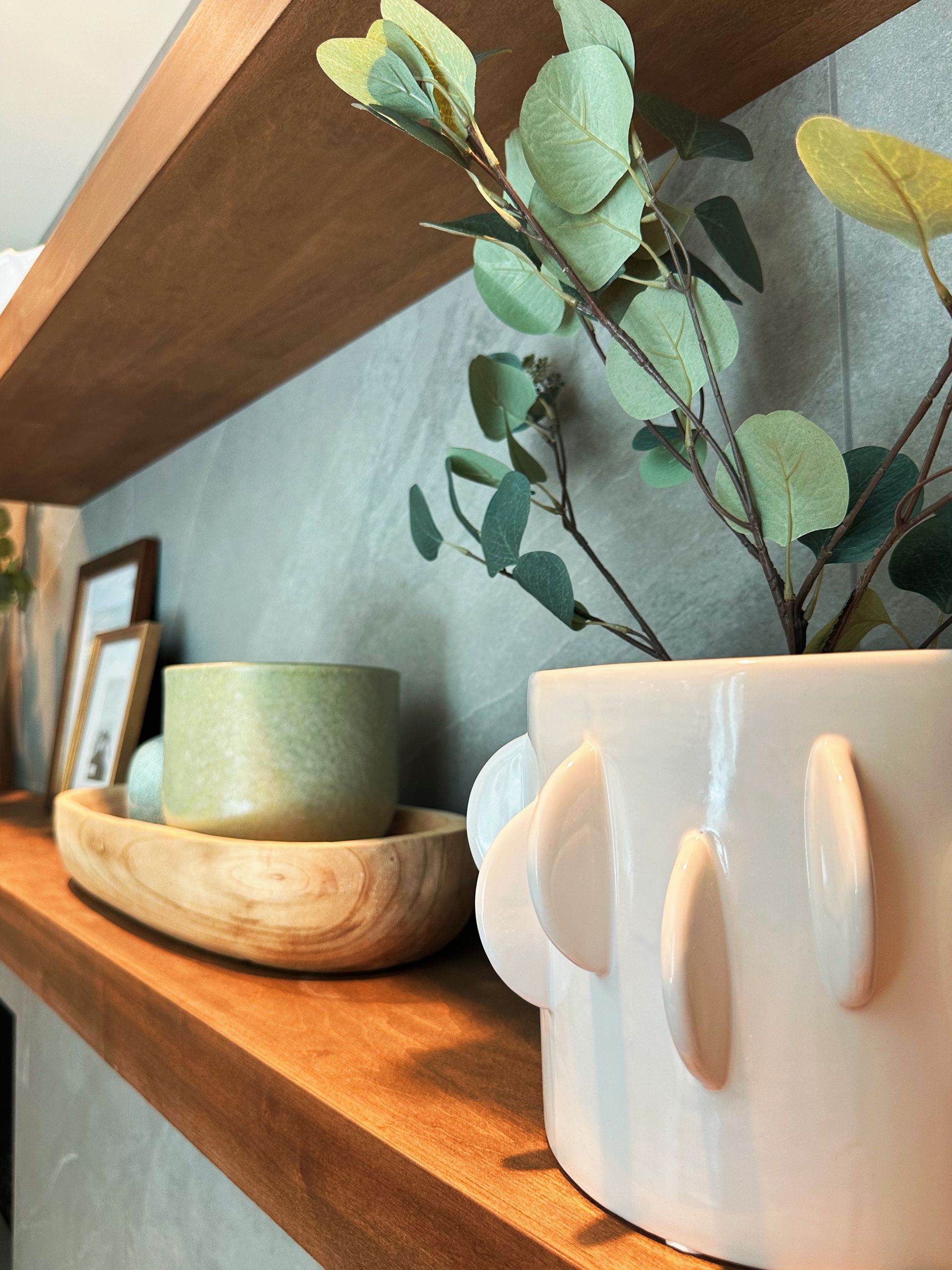 Wooden shelf with ceramic mugs, a candle, and leafy eucalyptus decor