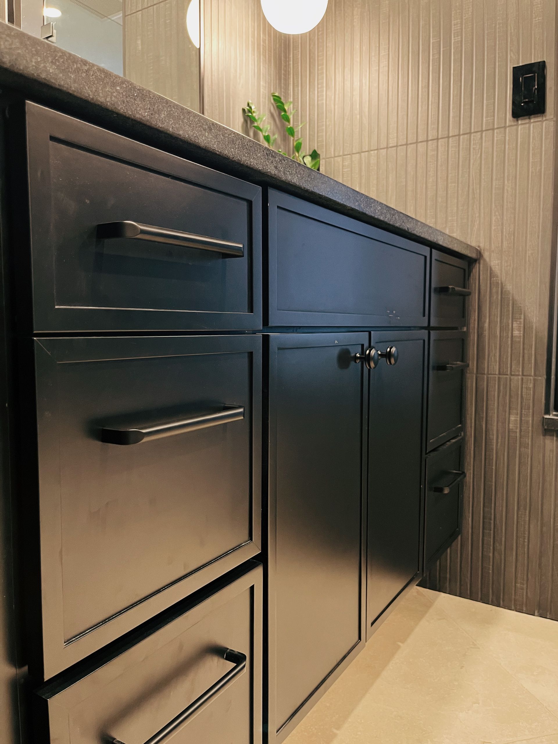 Black bathroom vanity with drawers and cabinet doors against wood-paneled wall, beige tile floor