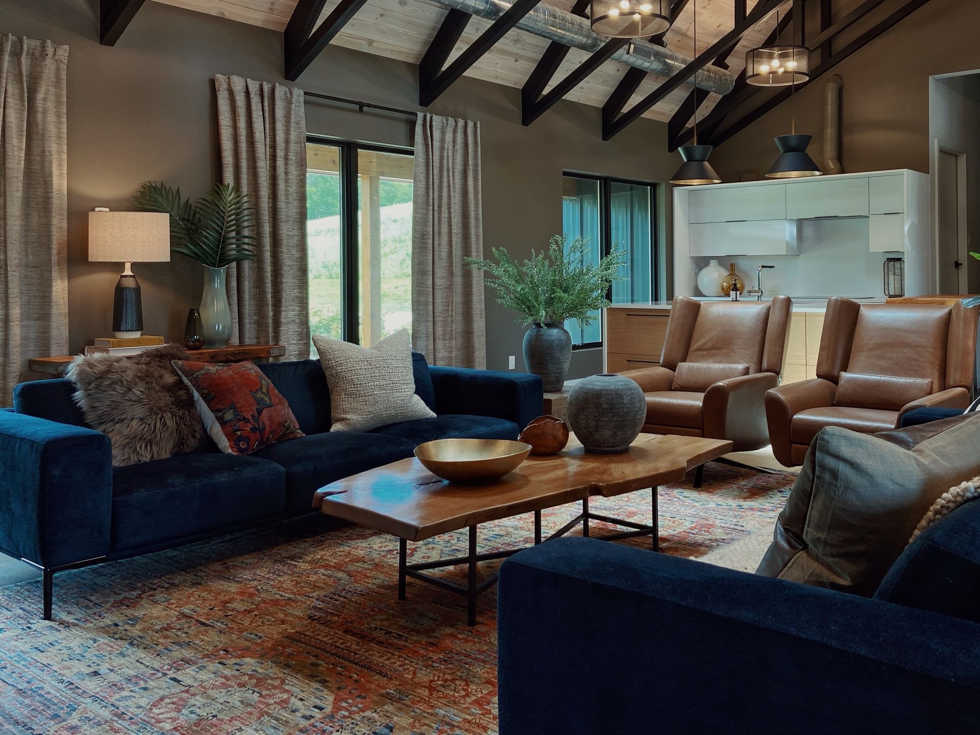 Elegant living room with navy sofas, tan chairs, wooden coffee table, and vaulted ceiling with exposed beams