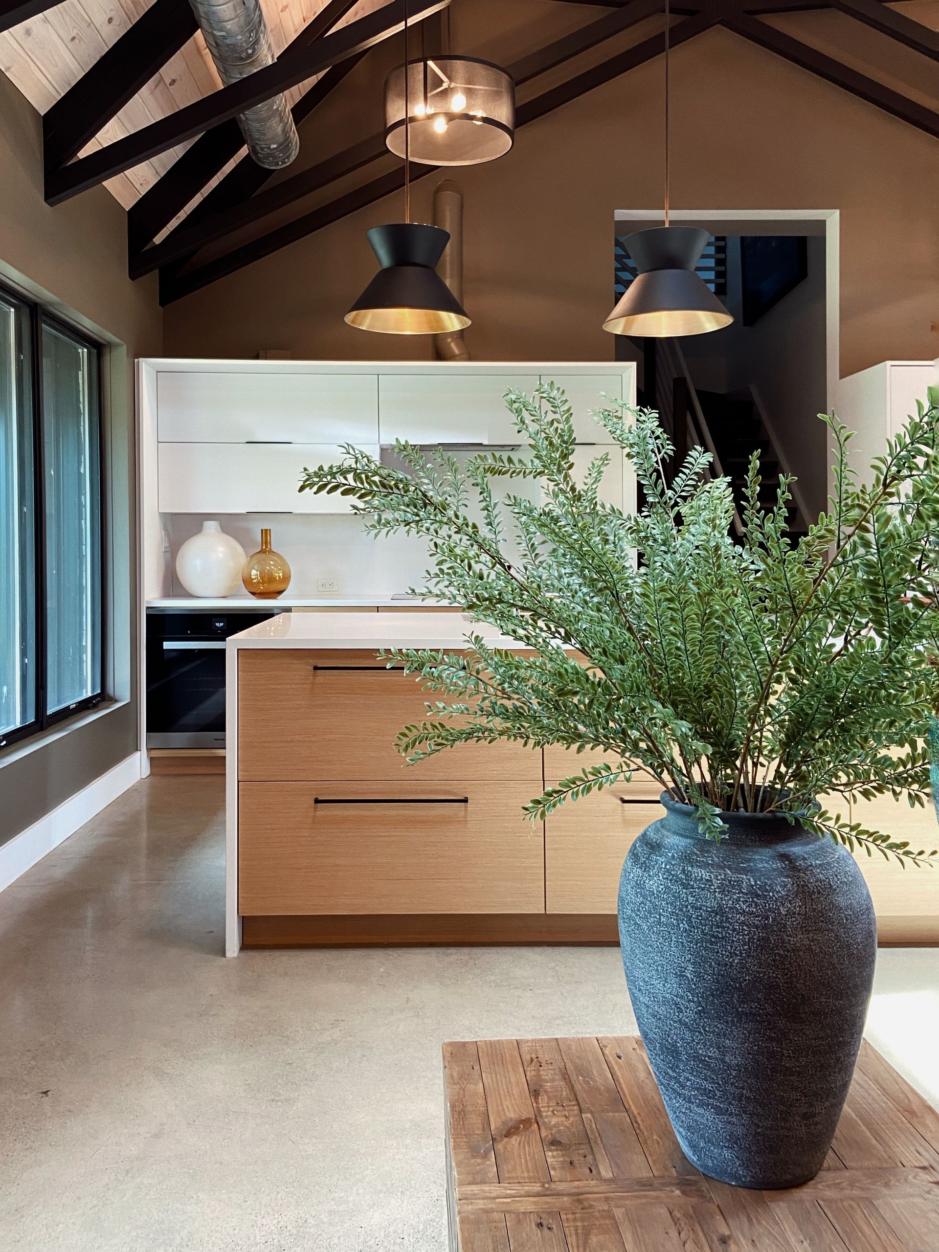 Modern kitchen with wood island, black pendant lights, and a large blue vase of greenery on a rug.