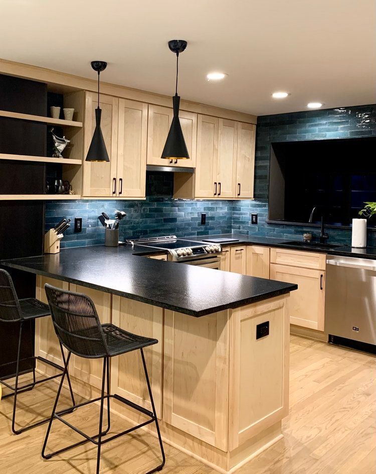 Modern kitchen with black island, light wood cabinets, pendant lights, and large window over sink