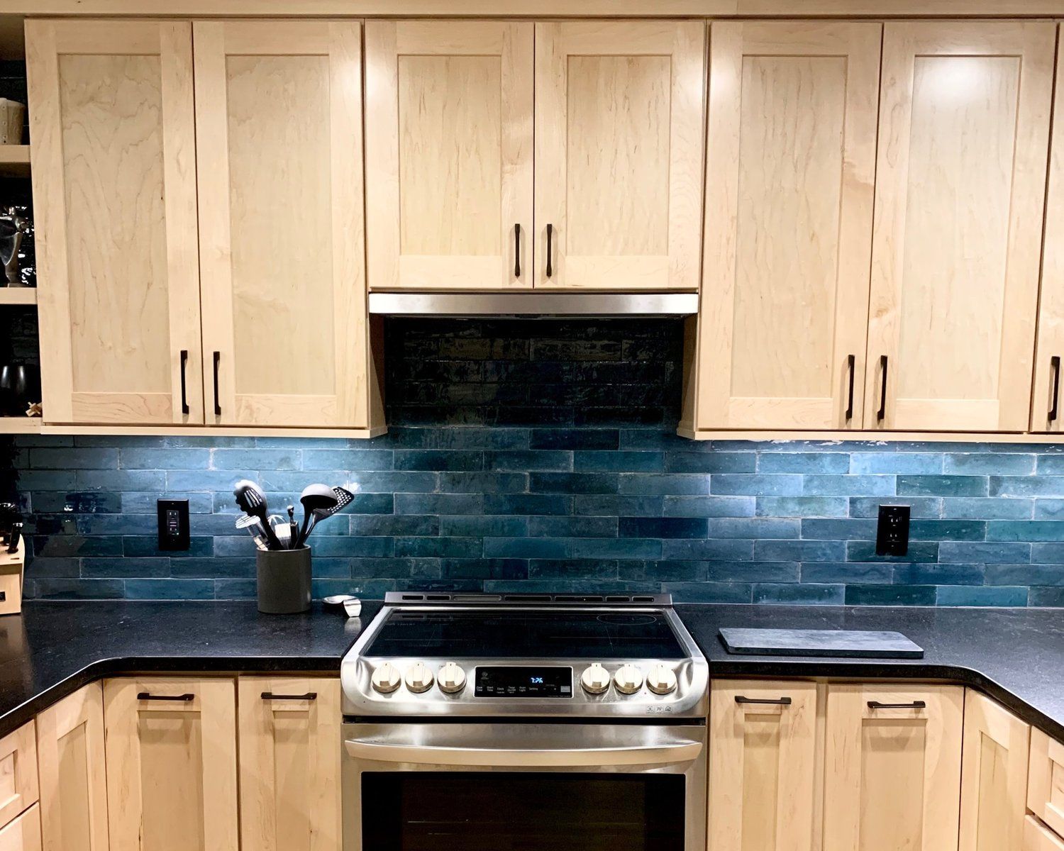 Modern kitchen with light wood cabinets, blue tile backsplash, and stainless steel stove and range hood.