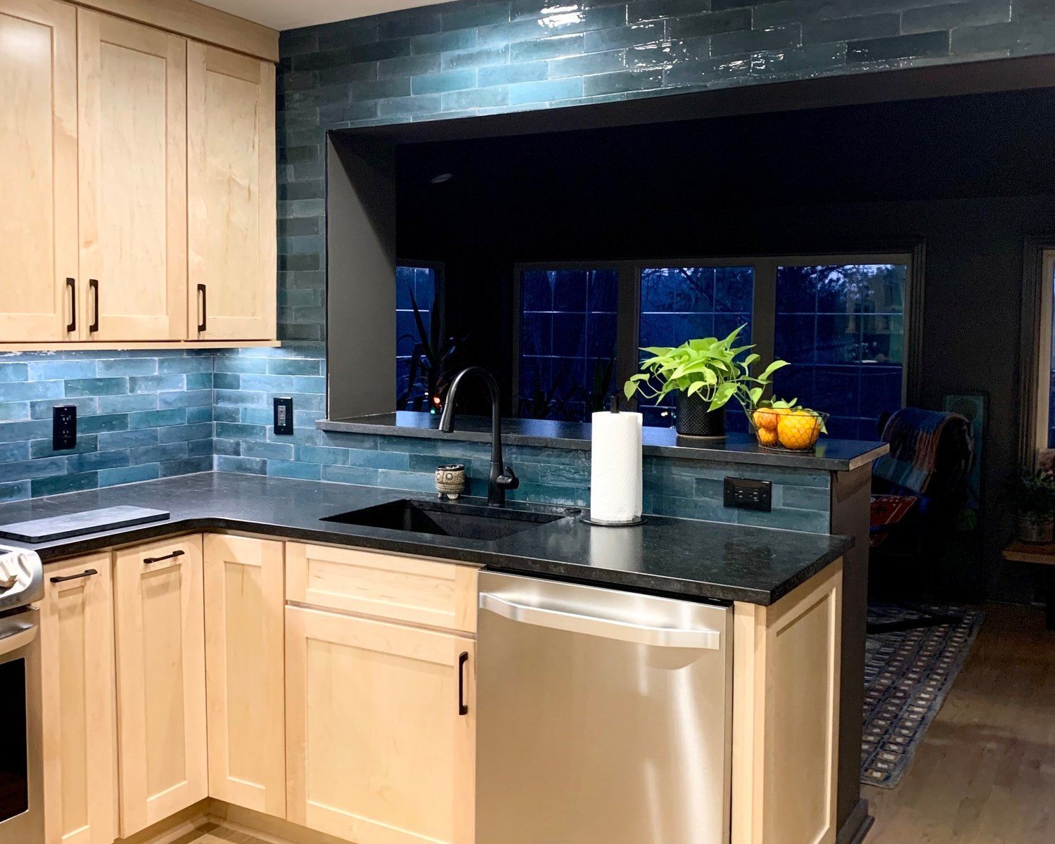 Modern kitchen with light wood cabinets, black granite island, stainless dishwasher, and blue tiled backsplash