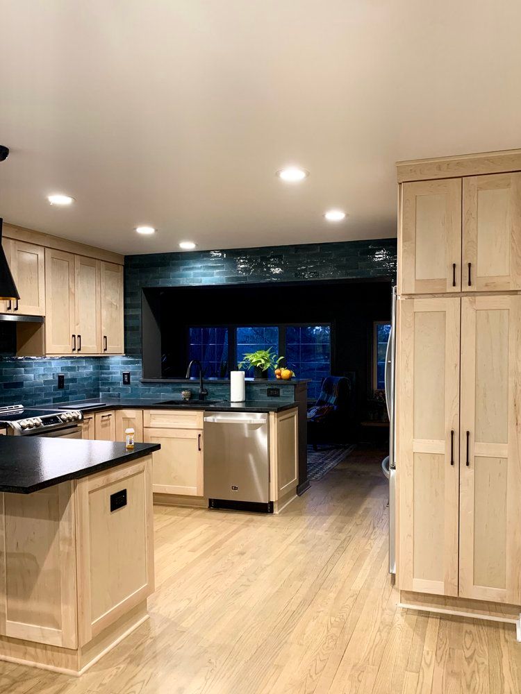 Bright modern kitchen with light wood cabinets, black countertops, and stainless steel appliances.