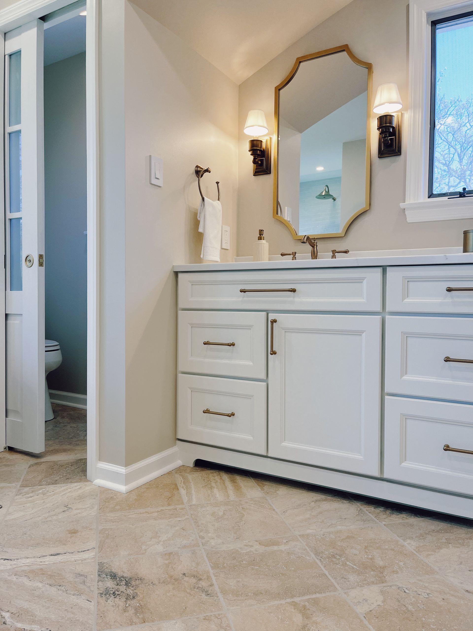 Bright bathroom with white vanity, large mirror, sconces, and marble tile floor