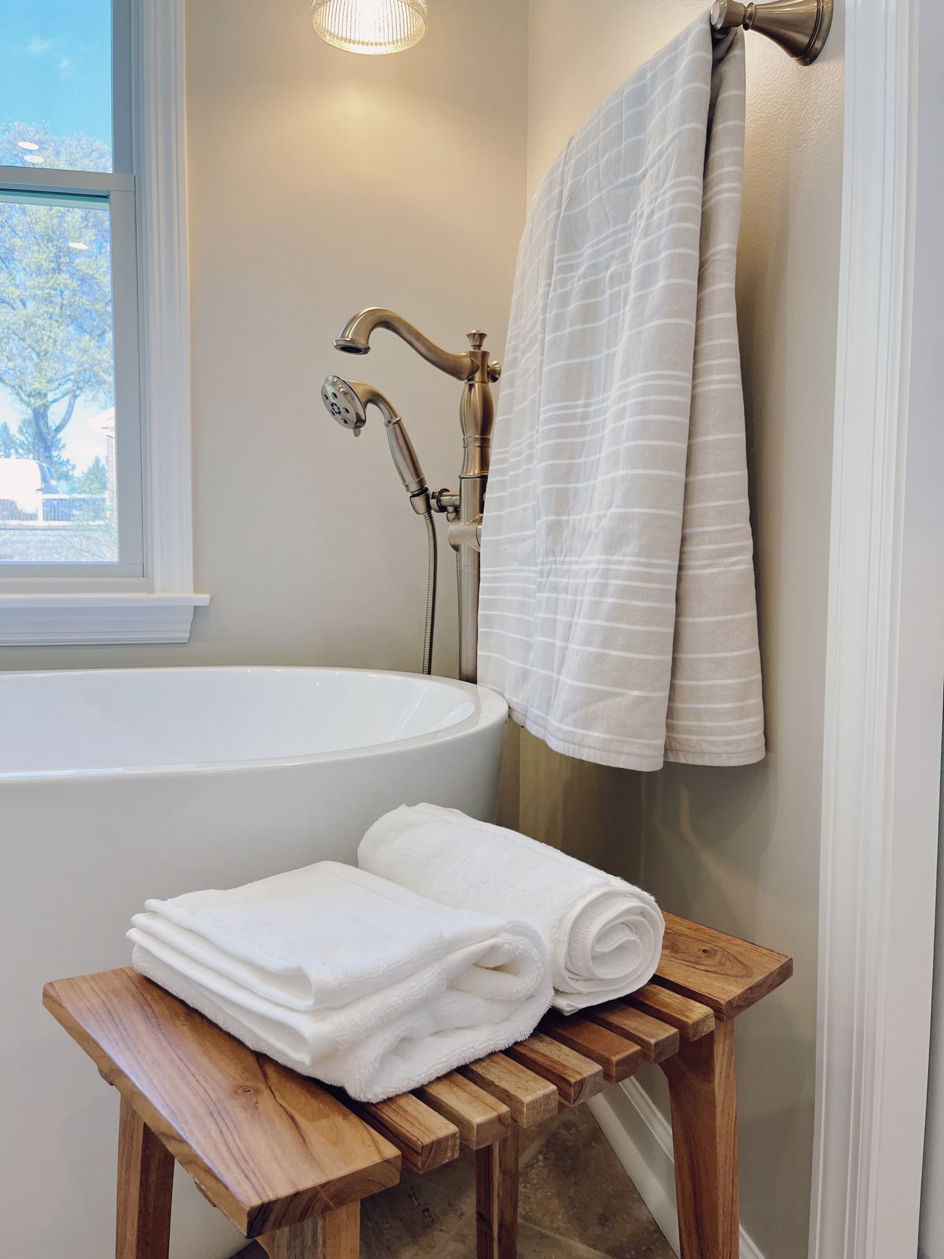 White towels on a wooden stool beside a bathtub in a bright bathroom