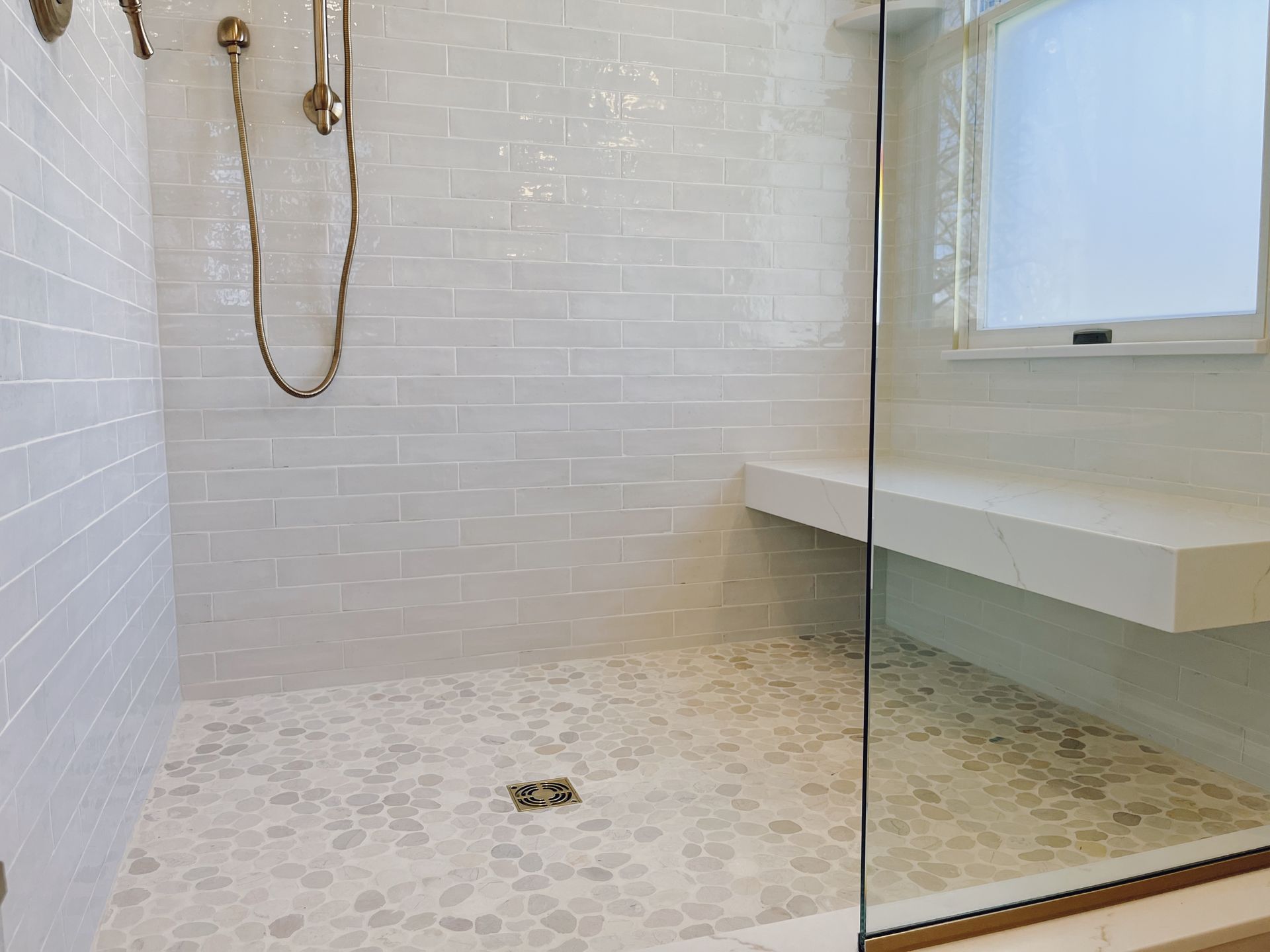 Glass shower with white tile walls, built-in bench, and chrome shower fixtures