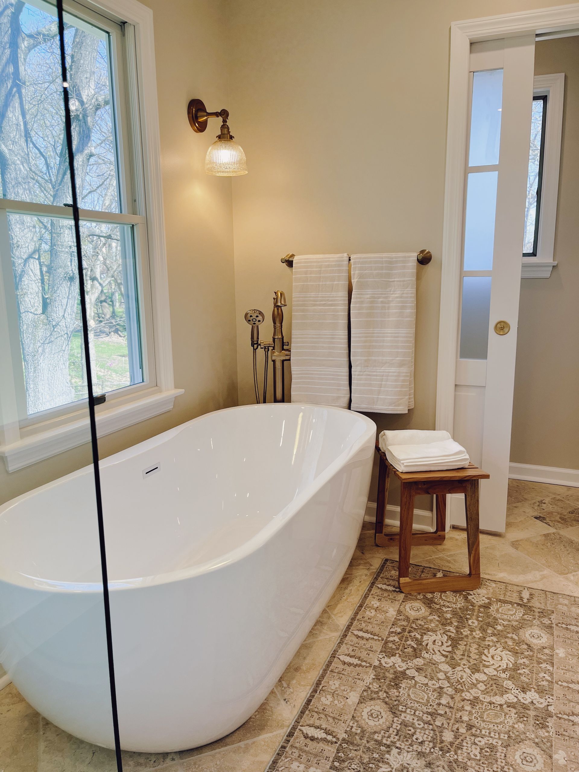 Bright bathroom with freestanding tub, window, towel rack, bench, and patterned rug