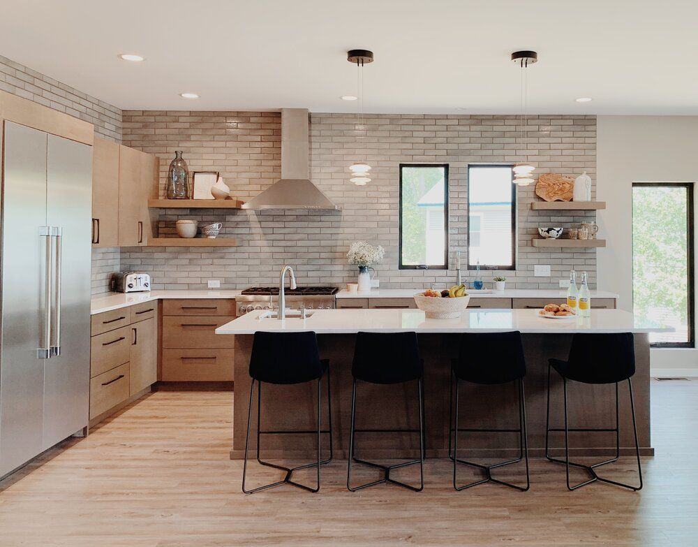 Modern open kitchen with light wood cabinets, marble island, black bar stools, and stainless steel appliances