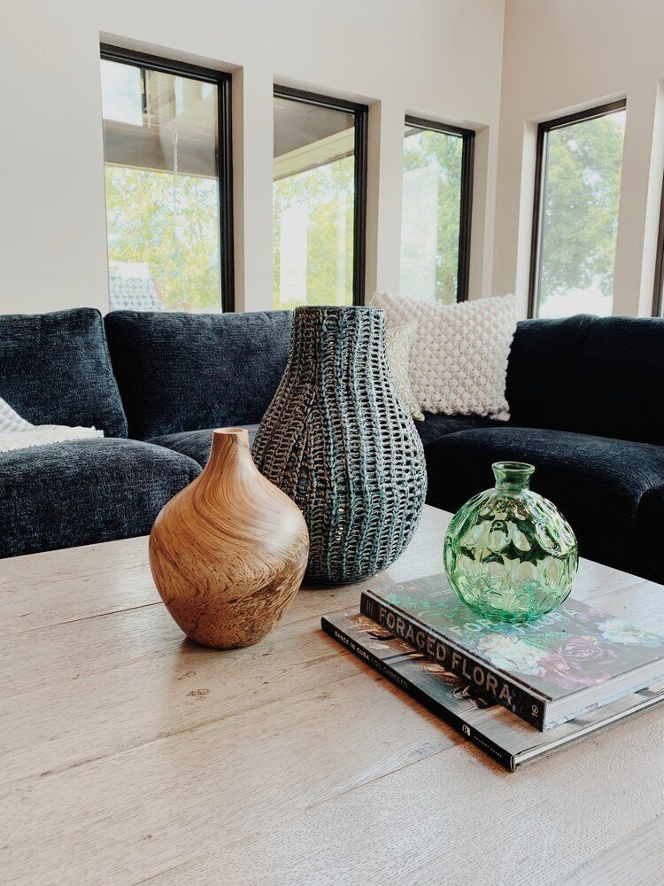 Living room with dark sofa, light wood table, and decorative vases by large windows