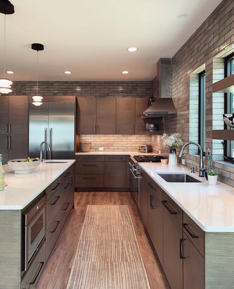 Modern kitchen with stainless steel appliances, dark wood cabinets, white countertops, and a brick accent wall.