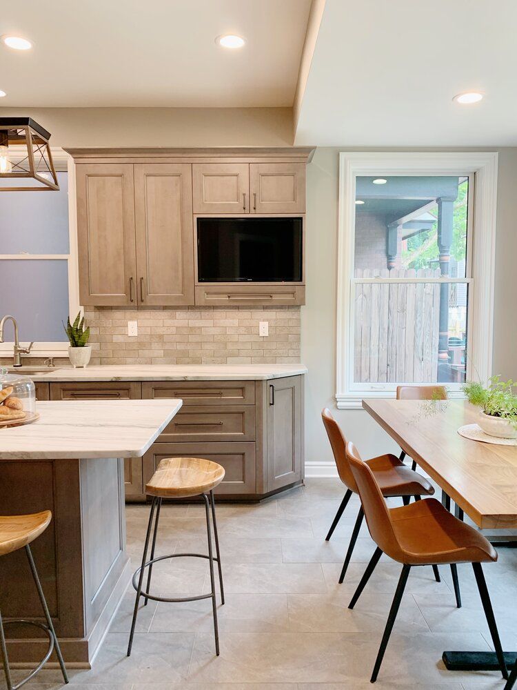 Bright modern kitchen with light wood cabinets, white countertops, and a dining table by a glass door.