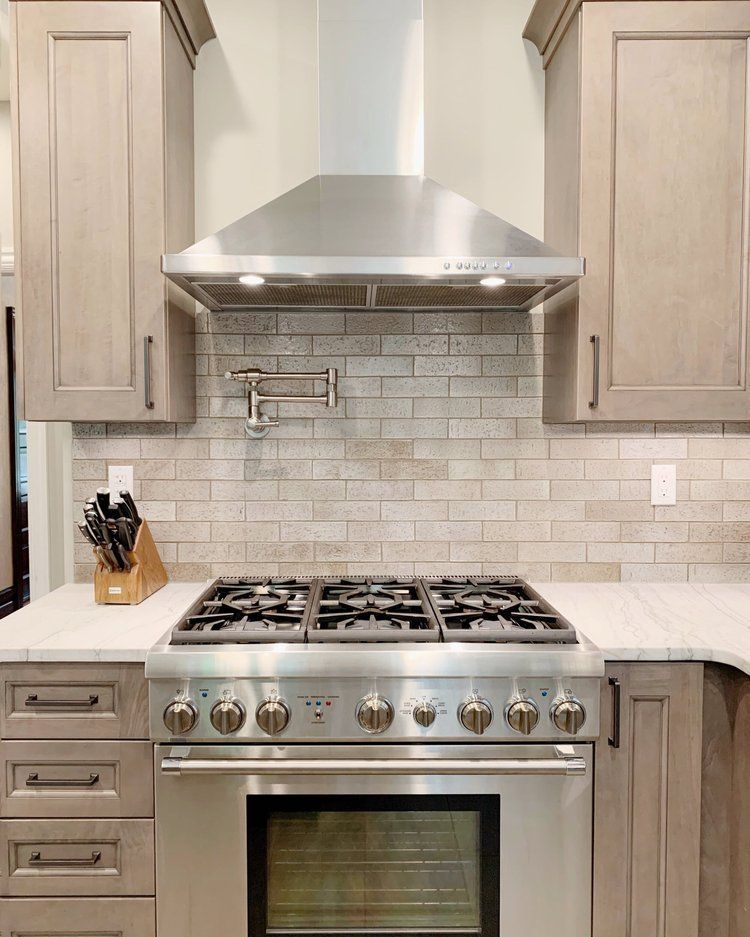 Modern kitchen with stainless steel gas range, range hood, and light wood cabinets