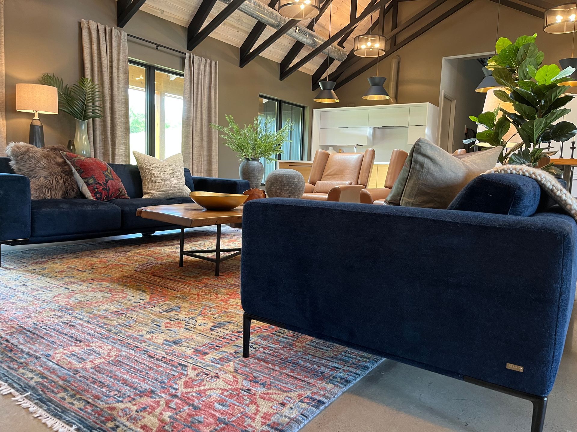 Cozy living room with navy sofas, colorful rug, exposed beams, and large windows