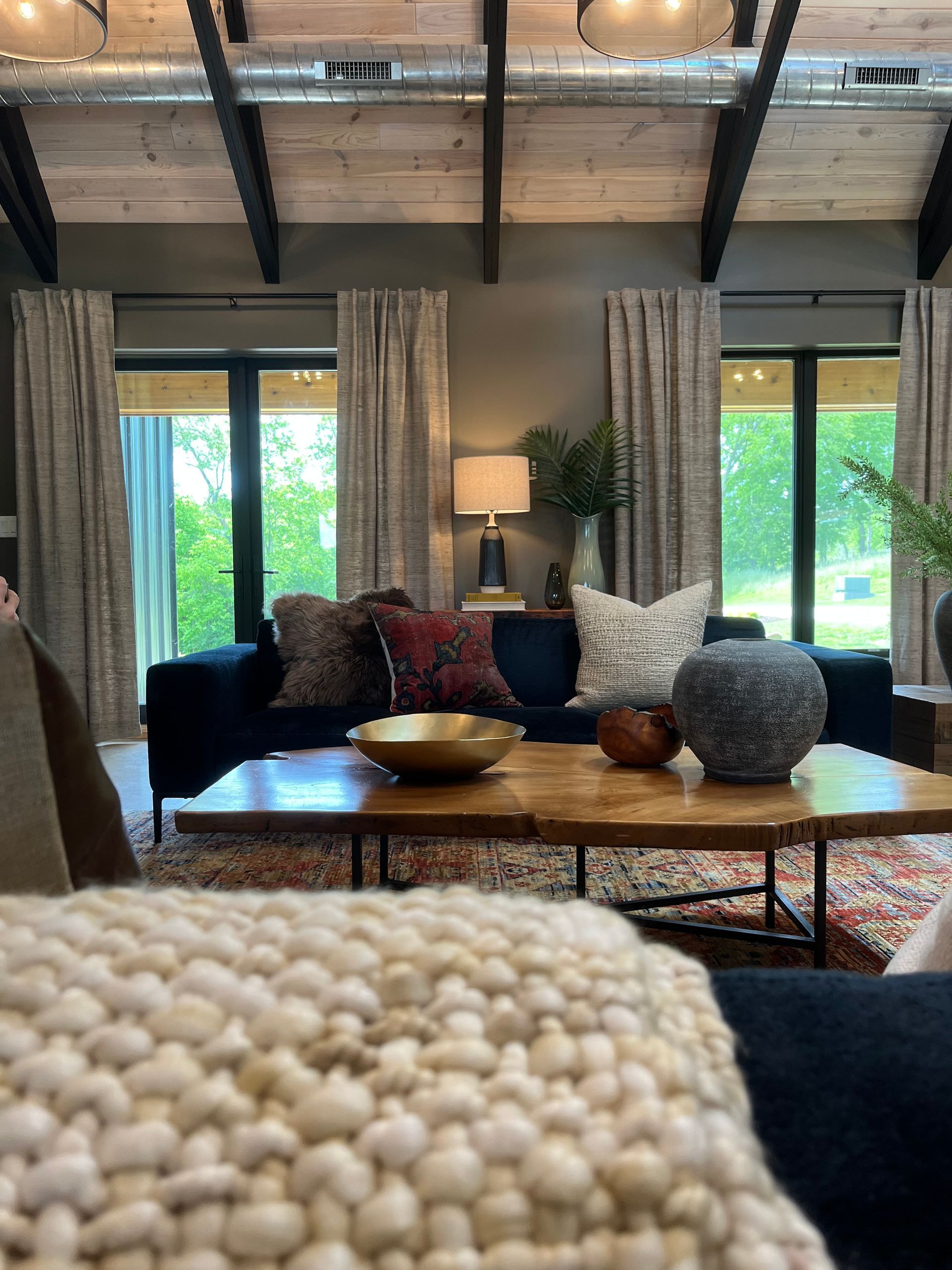 Cozy living room with dark sofa, wood coffee table, lamp, and large windows with curtains.