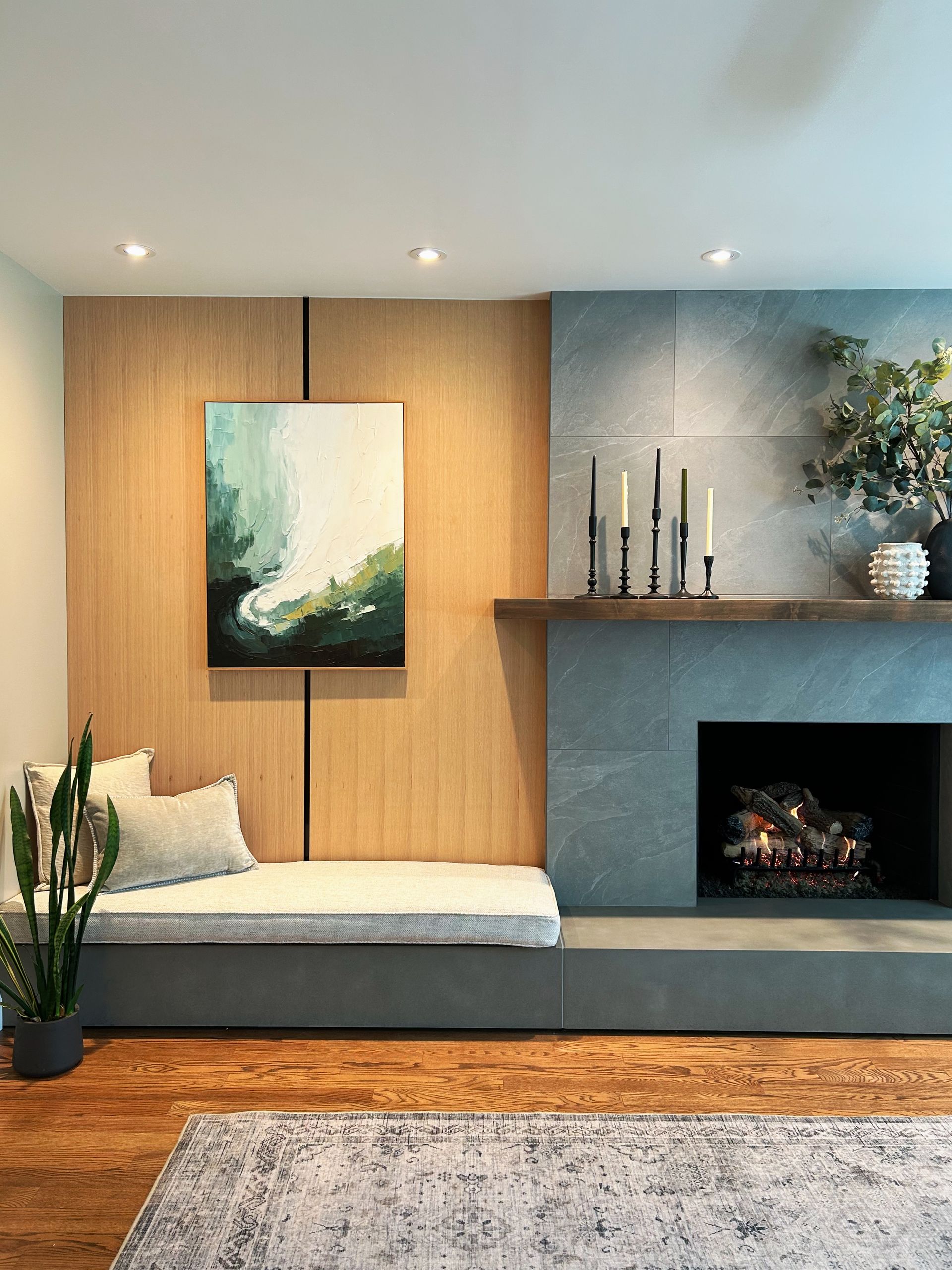 Modern living room with wood paneling, bench, fireplace, abstract art, and potted plant