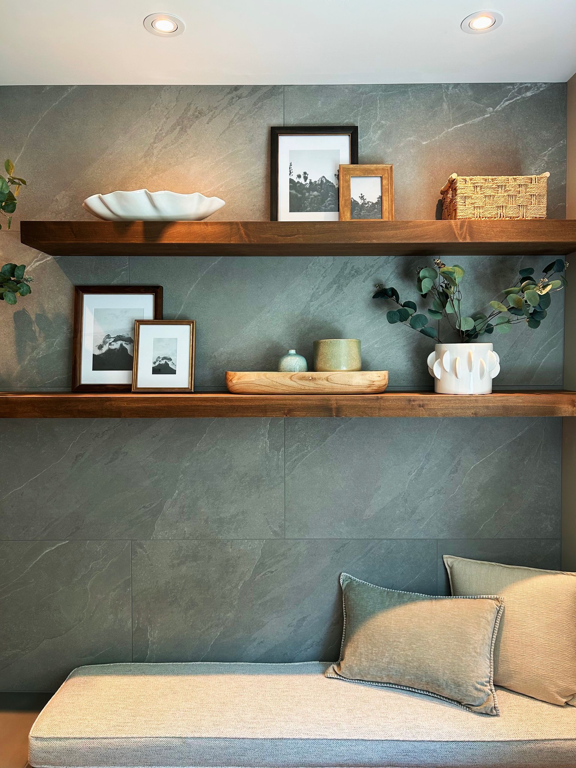 Modern built-in shelves with framed art, bowls, plants, and a cushioned bench in a gray wall niche