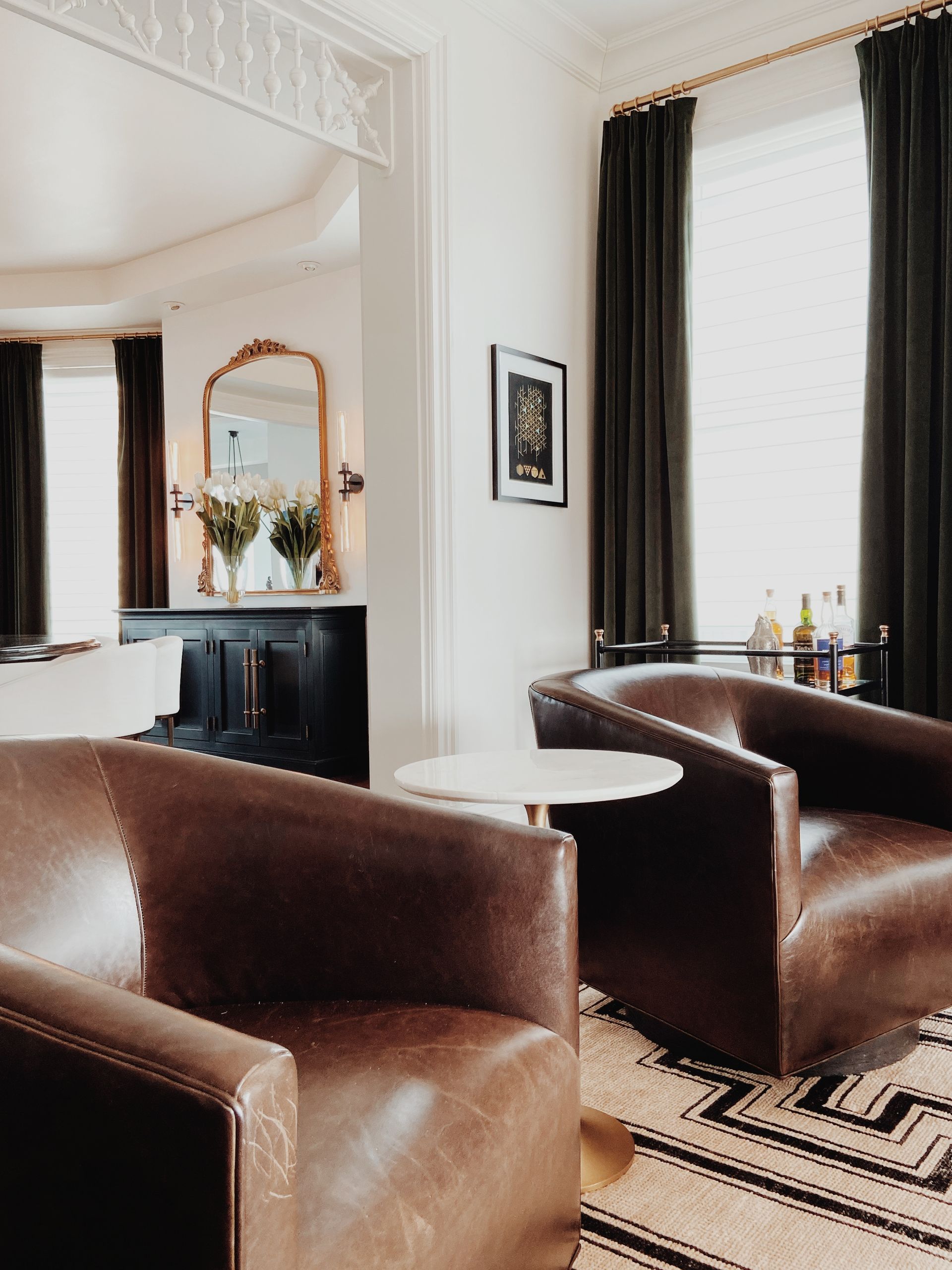 Elegant living room with brown leather chairs, mirrored console, and tall window with dark curtains
