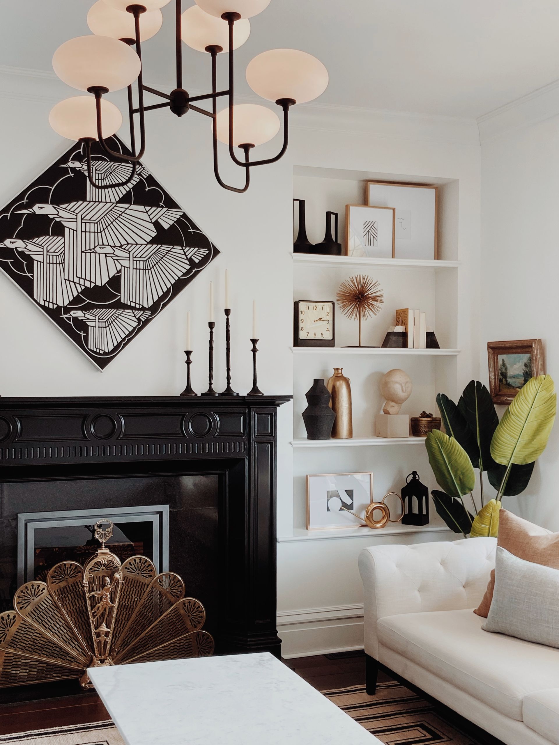 Elegant living room with black fireplace, white shelves, chandelier, and cream sofa with decorative pillows
