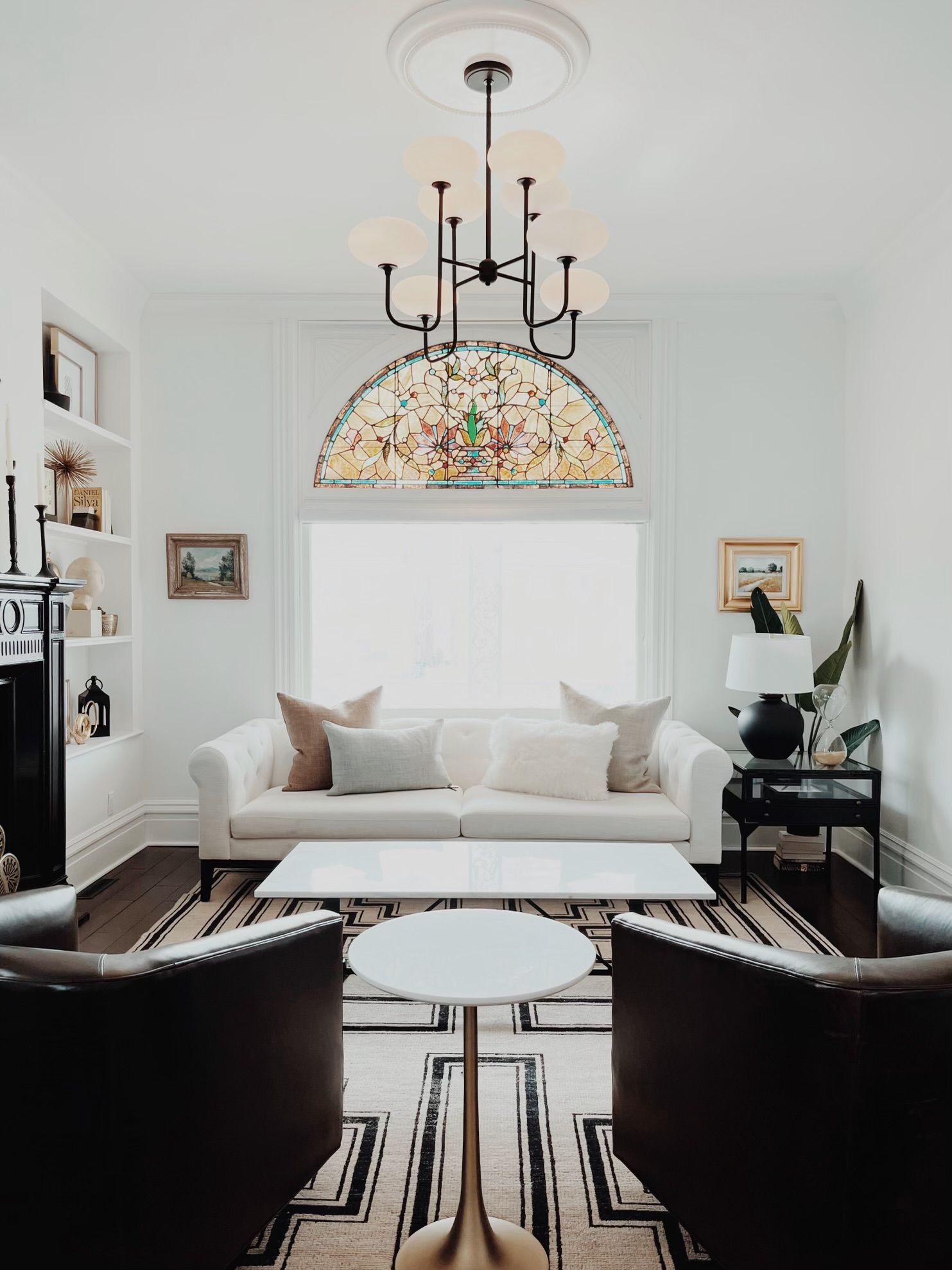 Elegant living room with white sofa, black chairs, patterned rug, and stained-glass chandelier