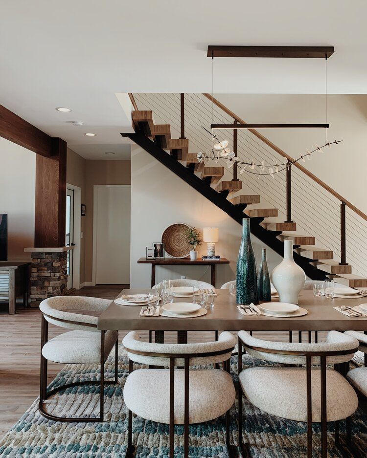 Modern dining room with round table, upholstered chairs, and open staircase with wood and black railings.