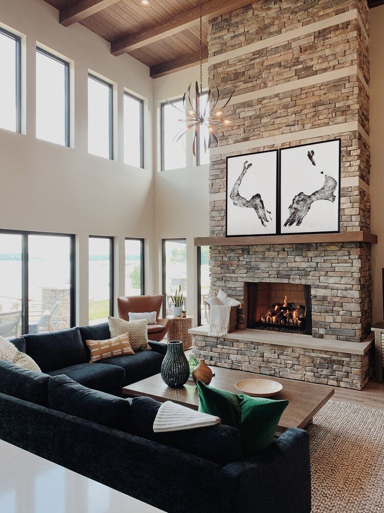 Modern living room with stone fireplace, high windows, and dark sectional sofa