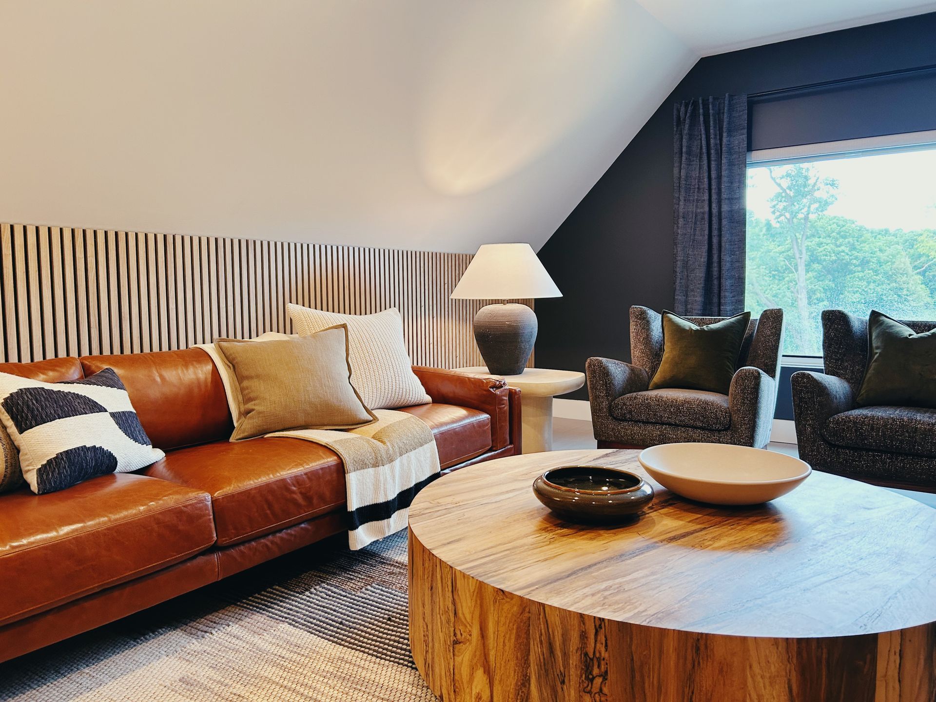Modern living room with leather sofa, patterned chairs, round wooden table, and large window